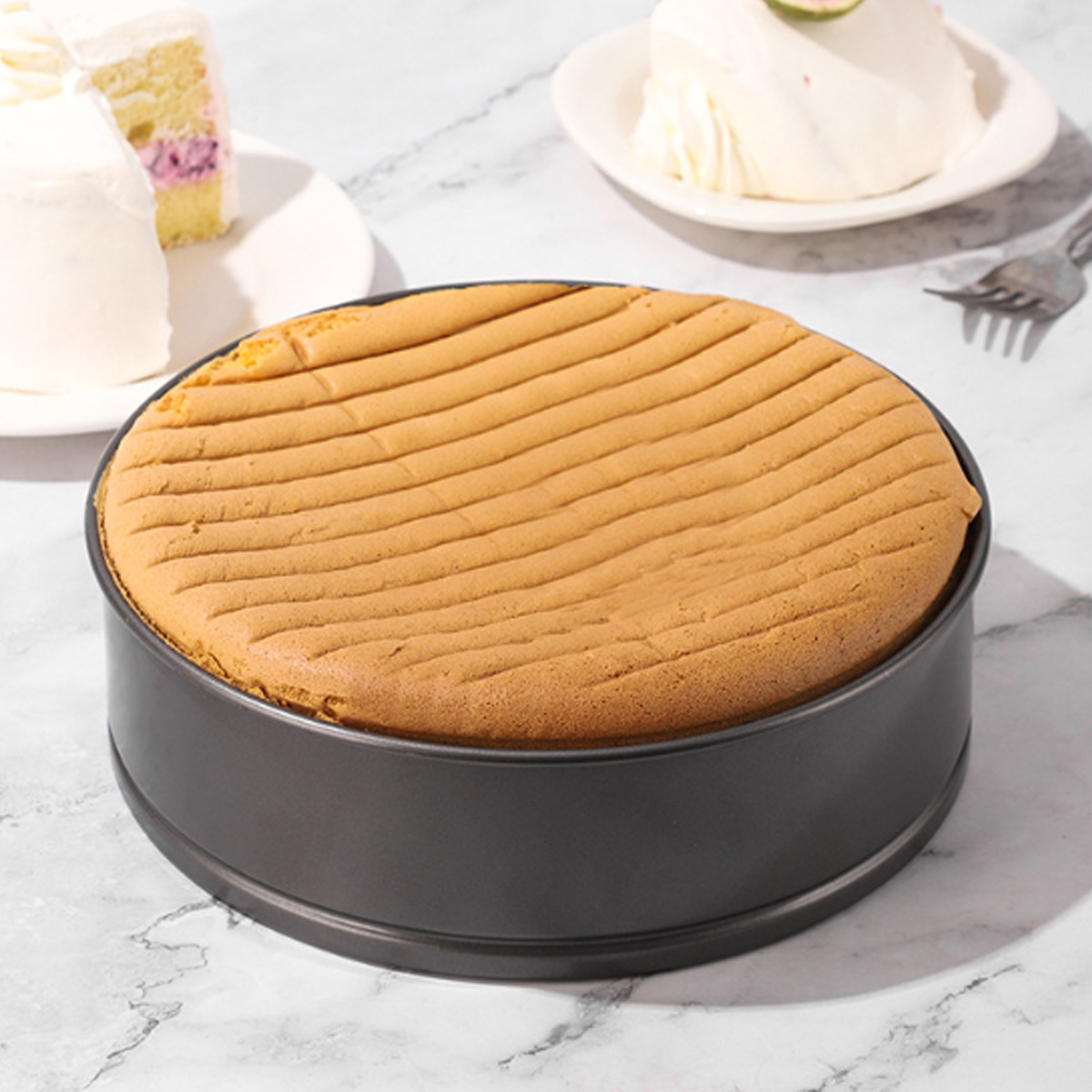 Ein runder Kuchen in einer Backform mit strukturierter Oberseite. Kuchenstücke auf Tellern im Hintergrund, auf Marmoroberfläche.