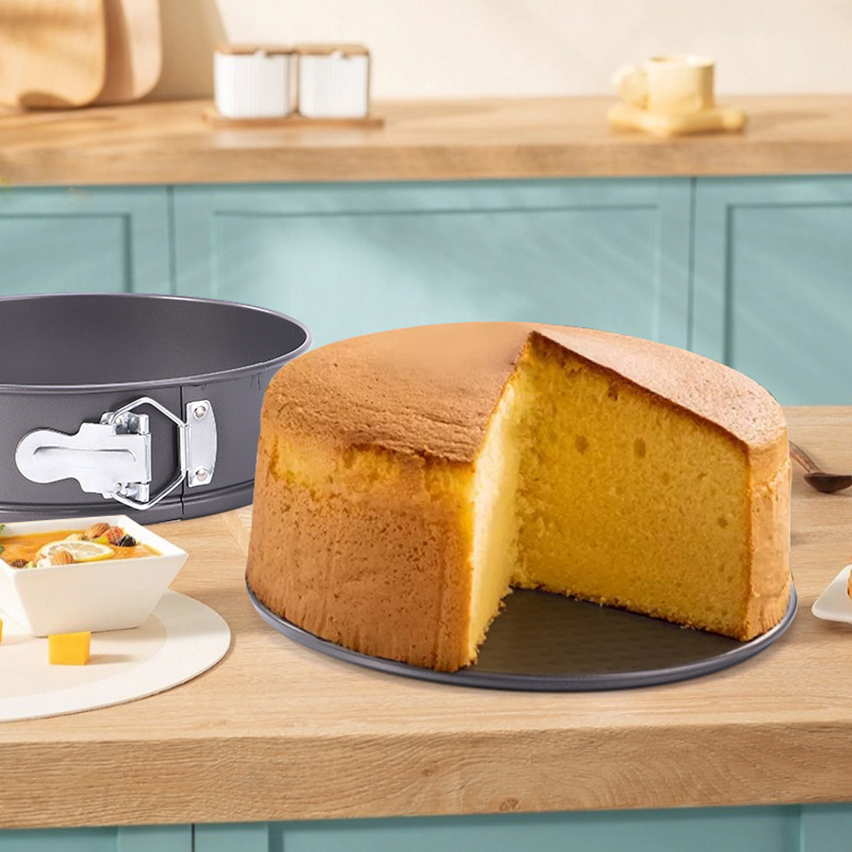 Ein Kuchen mit einem herausgeschnittenen Stück, der auf einem runden Teller liegt. Im Vordergrund befinden sich eine Kuchenform und eine kleine Schüssel mit Essen.