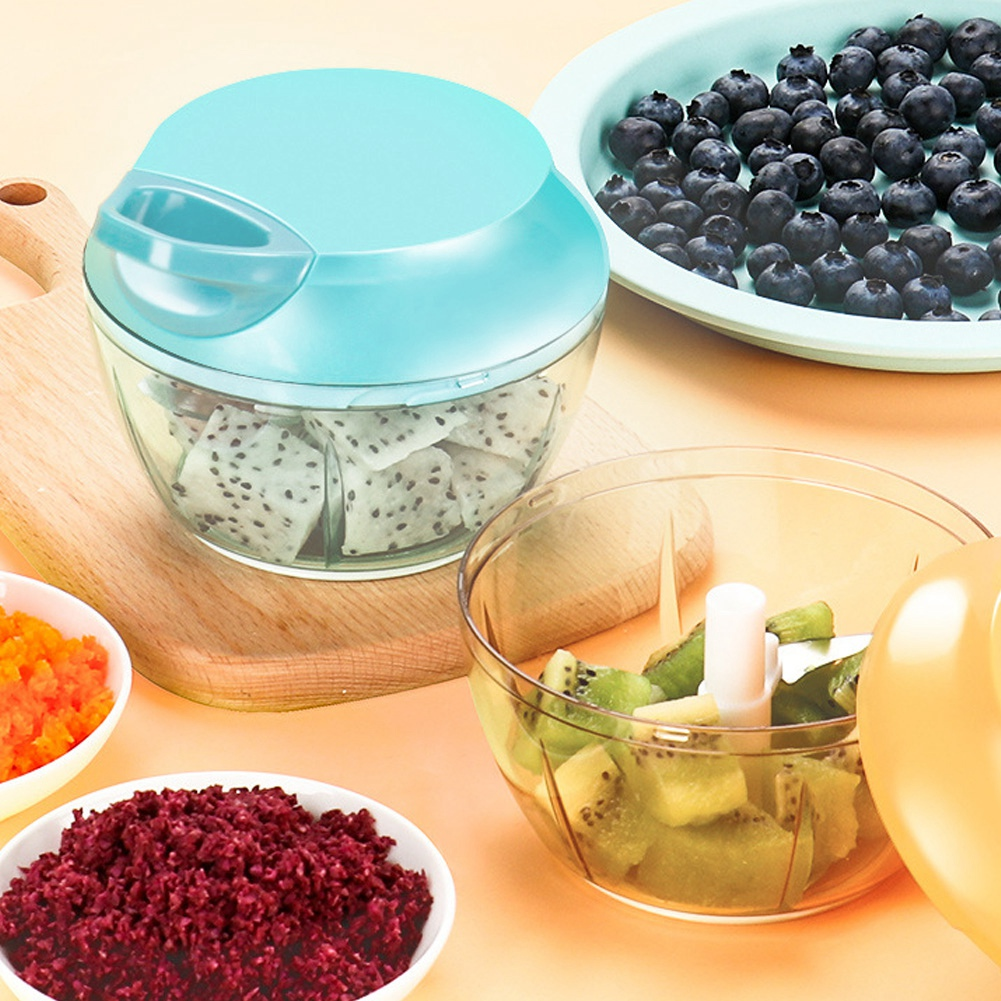 Ein manueller Zerkleinerer mit Drachenfrucht, Kiwi, Blaubeeren und anderem gehackten Gemüse. Schüsseln und ein Schneidebrett sind vorhanden.