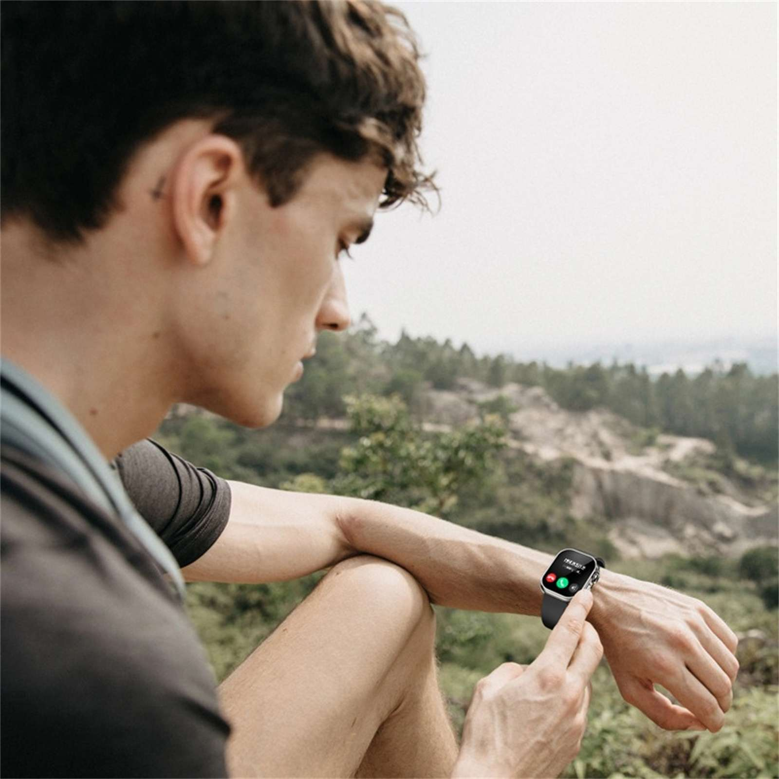 Mann, der im Freien auf eine Smartwatch schaut. Grüne und rote Anrufsymbole auf dem Bildschirm. Berge und Bäume im Hintergrund.