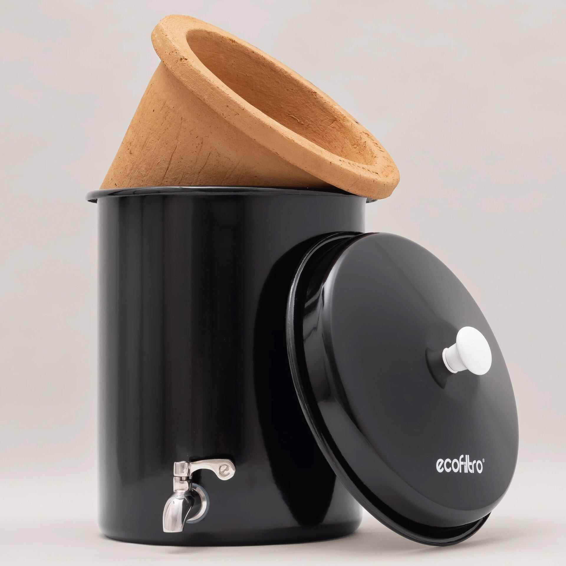 Un filtro per l'acqua nero con un filtro in terracotta sopra e il coperchio aperto di lato.
