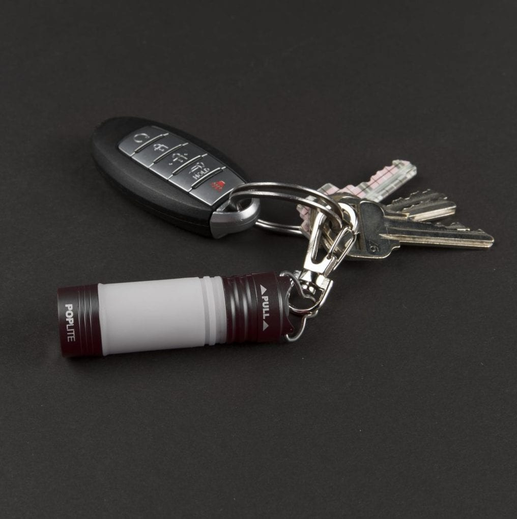 Schlüssel, ein Autoschlüssel und eine Poplite-Taschenlampe auf dunkler Oberfläche. Die Schlüssel sind silberfarben, der Autoschlüssel ist schwarz und die Leuchte ist weiß und rot.