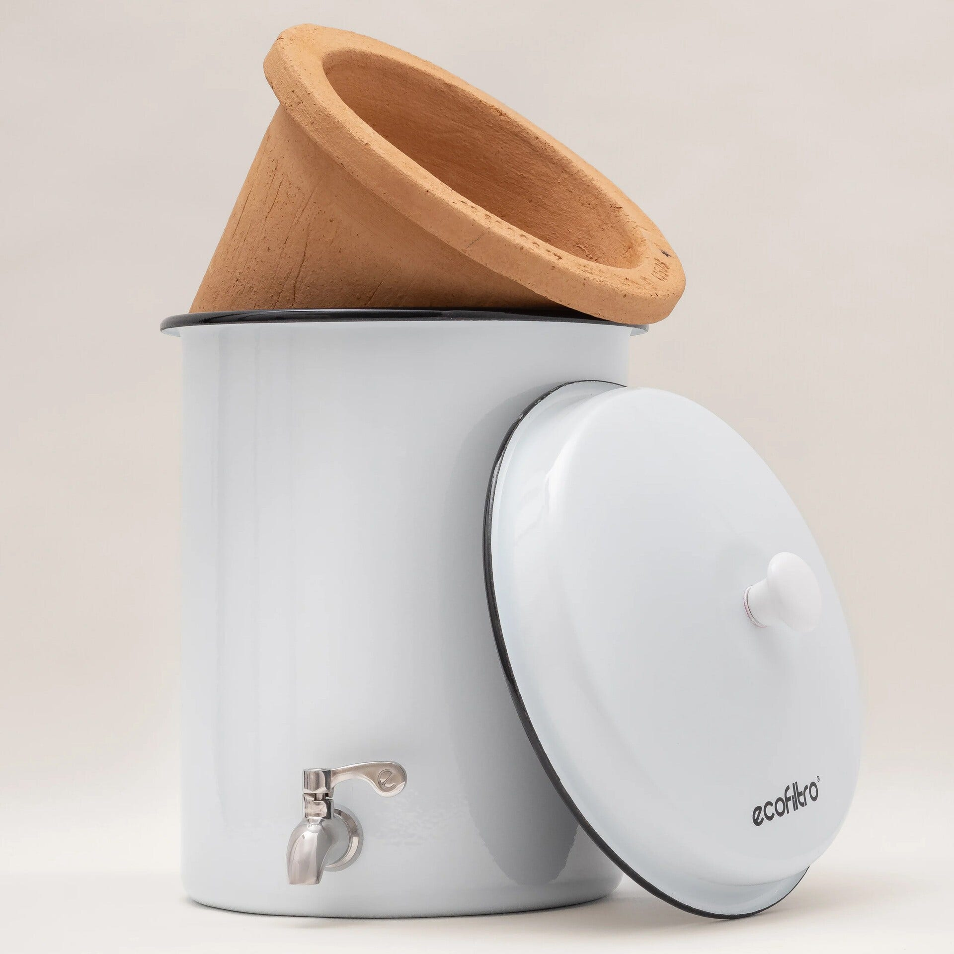 Un filtro per l'acqua bianco con un filtro in terracotta sopra e un coperchio bianco. Un rubinetto è visibile.