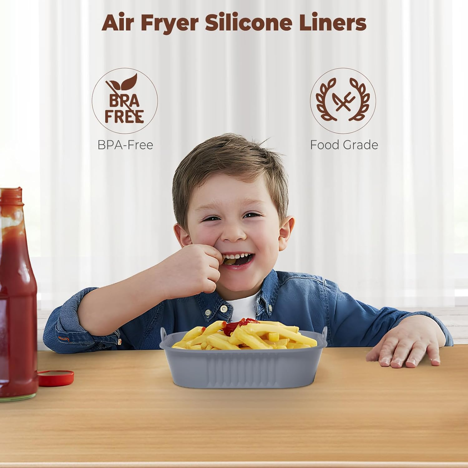 Ein lächelnder Junge isst Pommes aus einem grauen Behälter. Eine Ketchupflasche steht auf dem Tisch. Text: 'Air Fryer Silikon-Einsätze'.