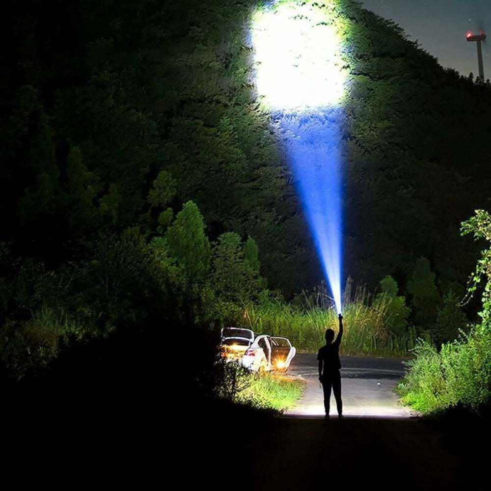 Eine Person hält eine Taschenlampe und leuchtet einen blauen Strahl in den Nachthimmel. Autos stehen auf einer Straße, umgeben von Bäumen.
