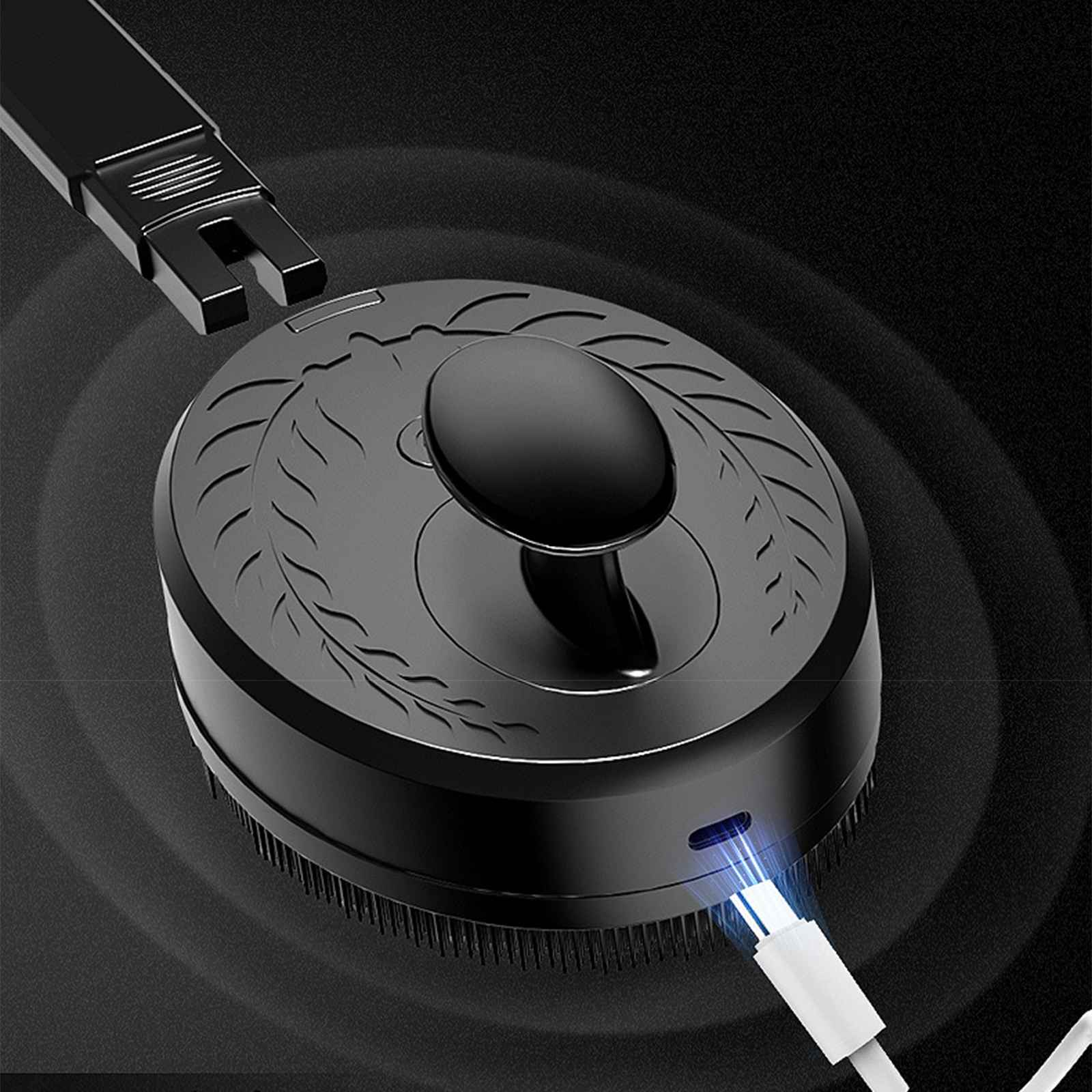 Ein schwarzes Pflegegerät mit Griff und Borsten. Ein Ladekabel ist angeschlossen. Ein schwarzes Teil ist abgetrennt.