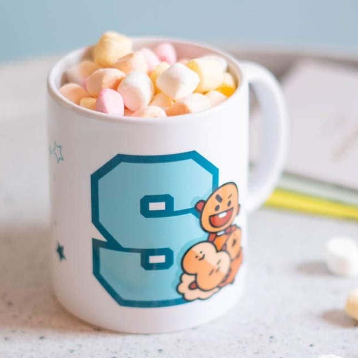 Weißer Becher gefüllt mit bunten Marshmallows. Der Becher hat die Zahl 9 und eine Cartoonfigur.