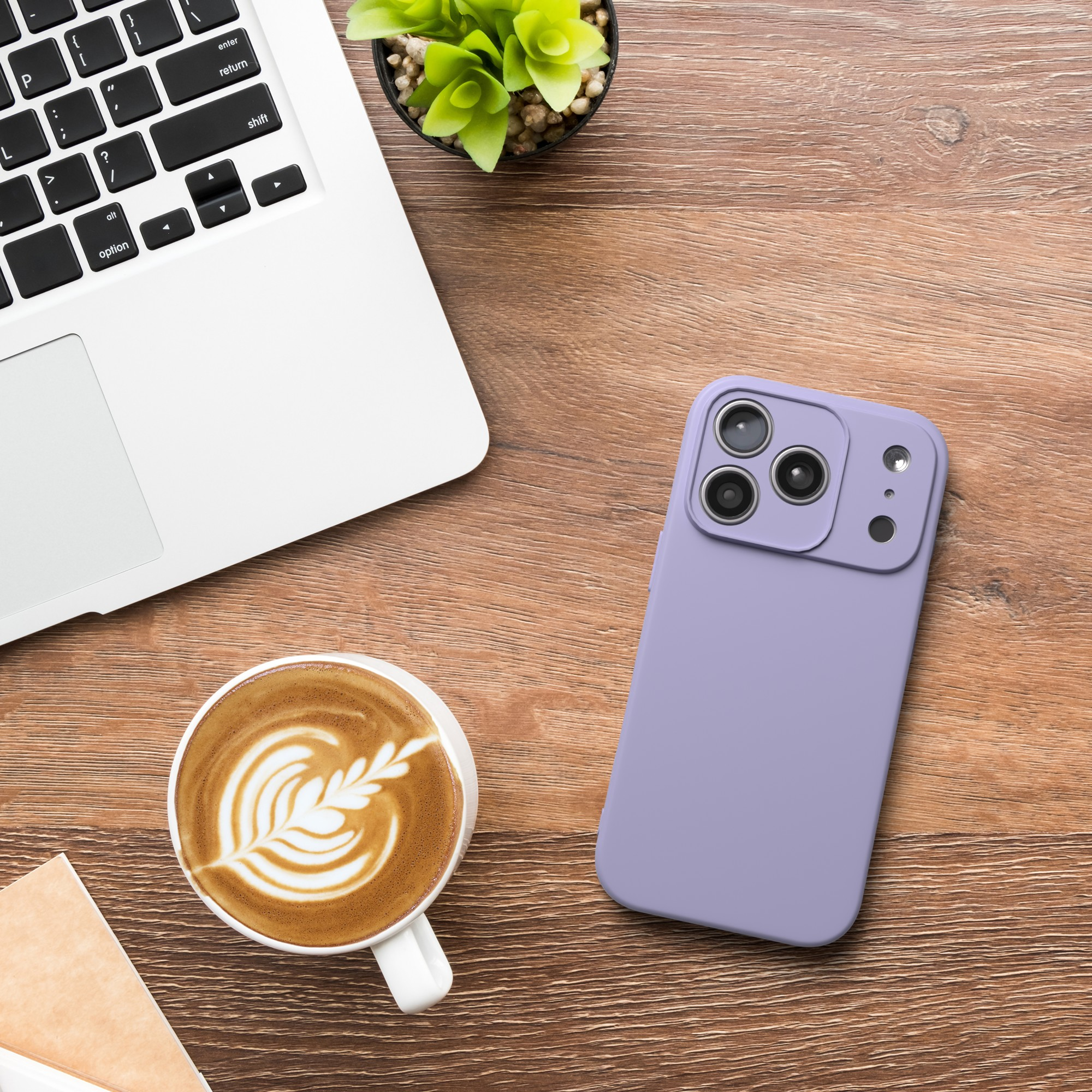 Ein Laptop, eine Tasse Kaffee mit Latte Art und eine lila Handyhülle auf einem Holztisch.
