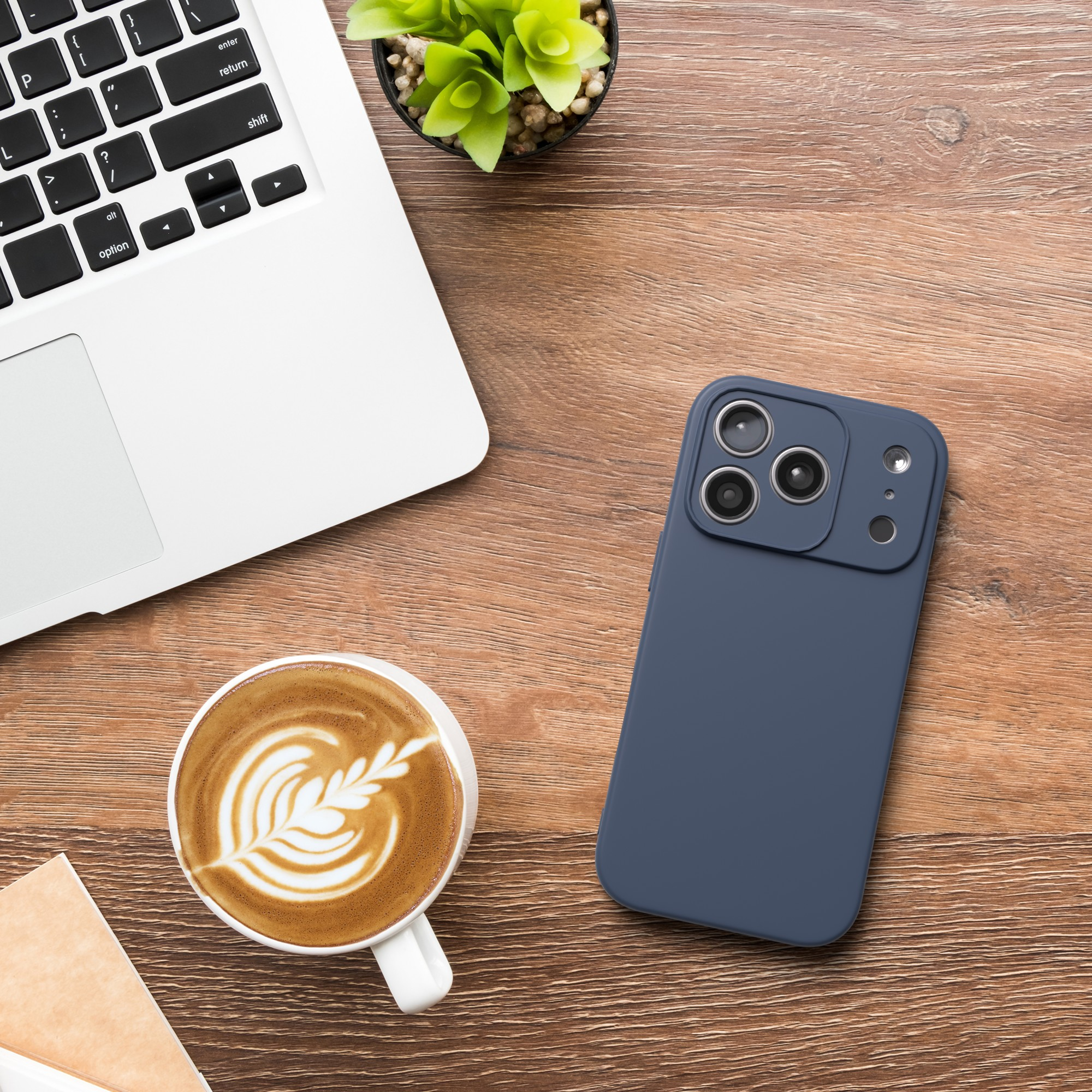Laptop, Kaffee mit Latte Art, blaues Telefon und eine kleine Pflanze auf einem Holzschreibtisch.