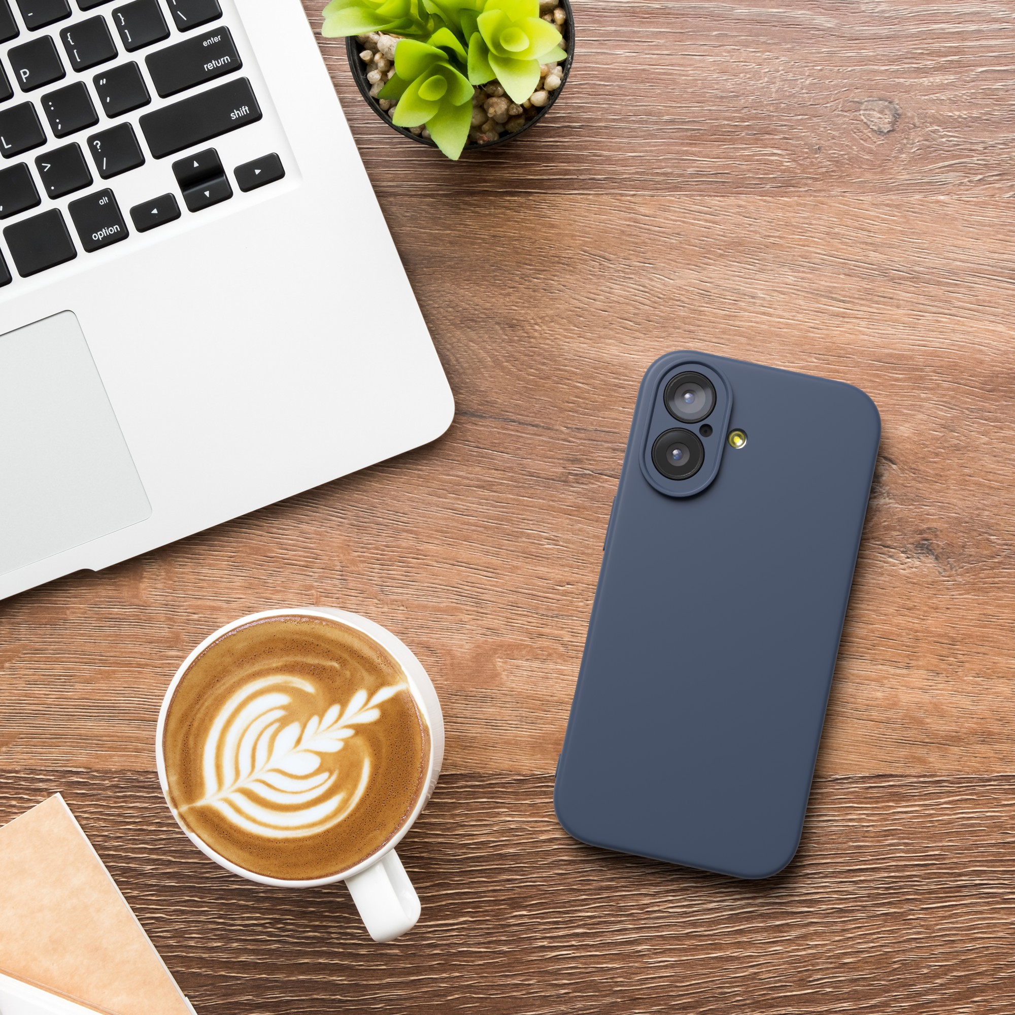 Ein Laptop, Kaffee mit Latte Art, ein blaues Telefon und eine Pflanze stehen auf einem Holztisch.