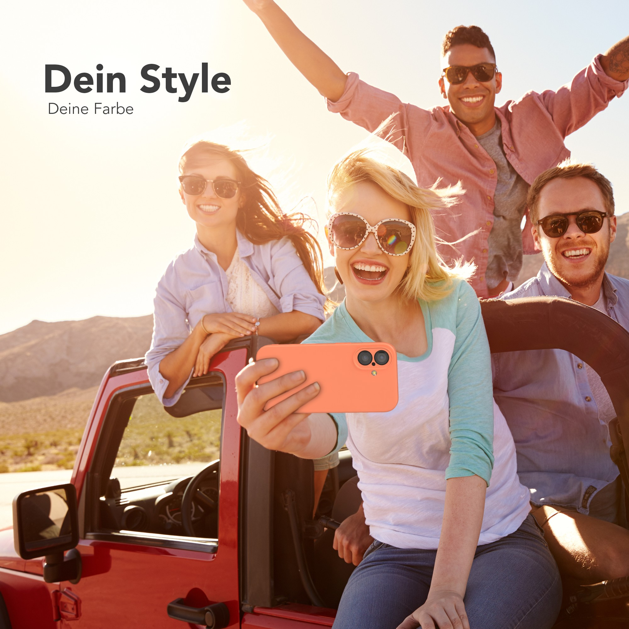 Vier lächelnde Personen machen ein Selfie aus einem roten Jeep. Einer hält ein Telefon. Wüstenhintergrund, sonniger Tag.