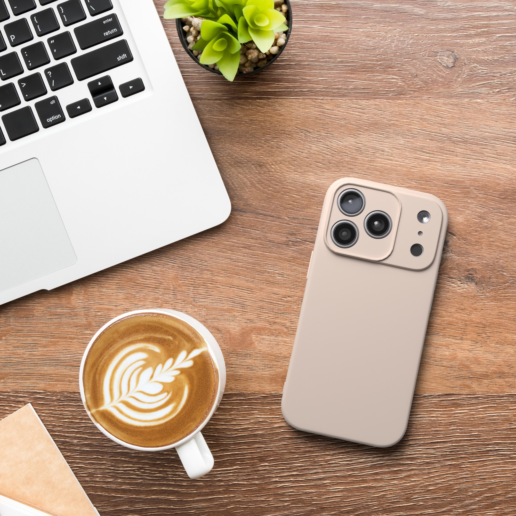 Ein Laptop, eine Kaffeetasse, ein Telefon und eine kleine Pflanze stehen auf einem Holzschreibtisch. Kaffee hat Latte Art. Telefon ist hellbraun.