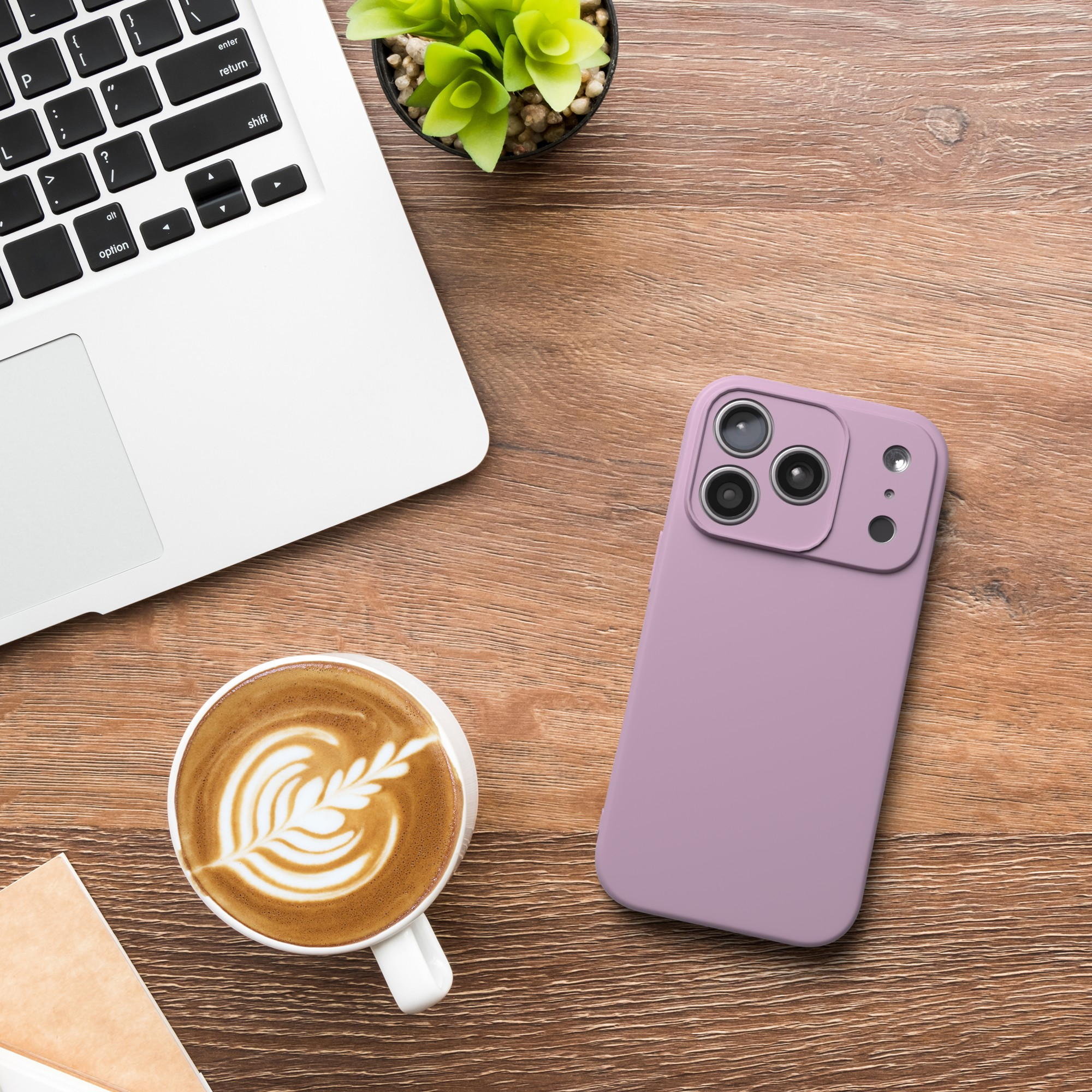 Laptop, Kaffee, Telefon mit Hülle auf einem Holztisch. Pflanze und Notizblock sind ebenfalls vorhanden.