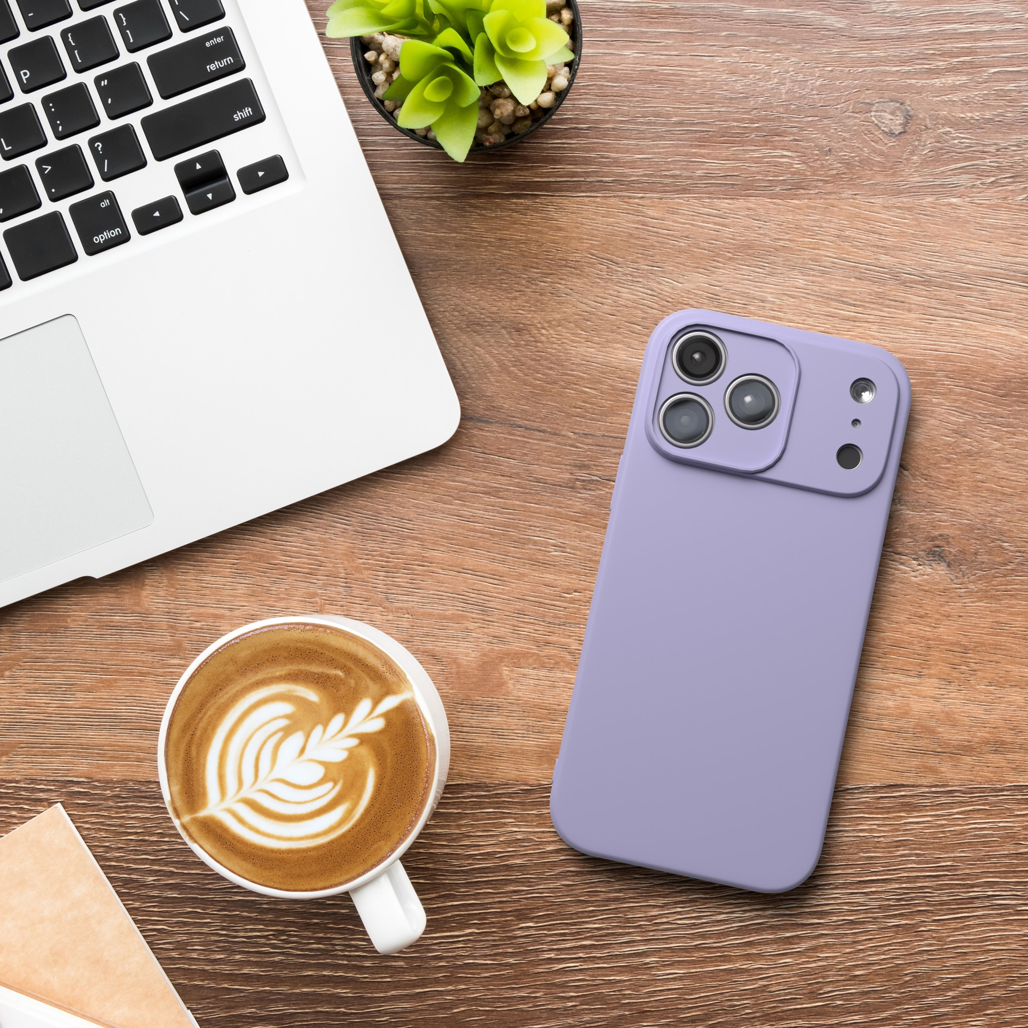 Ein Laptop, ein lila Telefon, eine Kaffeetasse mit Latte Art und eine kleine Pflanze auf einem Holztisch.