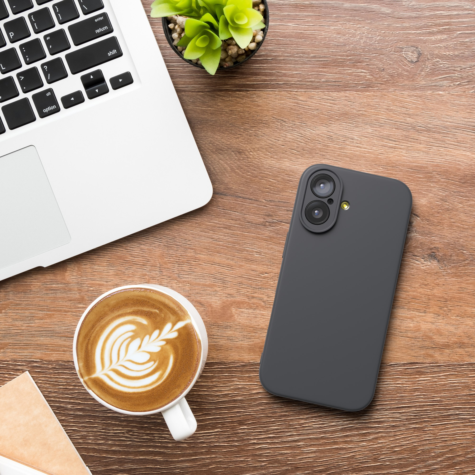 Ein Laptop, eine Tasse Kaffee mit Latte Art, ein Telefon und eine kleine Pflanze stehen auf einem Holztisch.