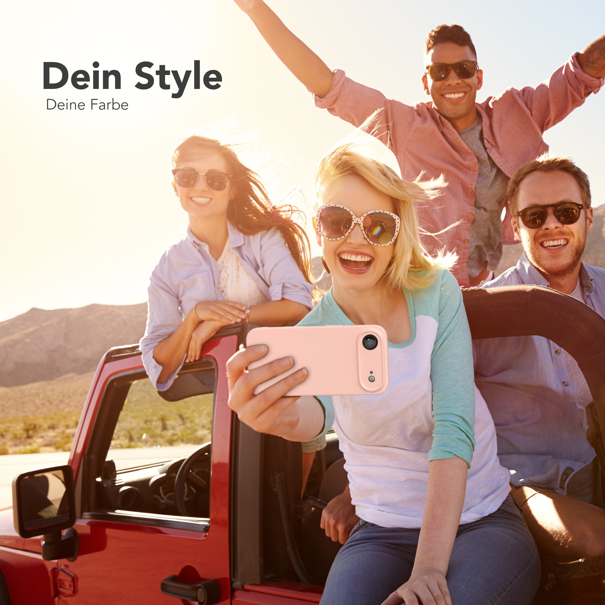 Vier Personen in einem roten Jeep machen ein Selfie. Sonniger Tag, Wüstenhintergrund. Lachende Gesichter, Sonnenbrillen.