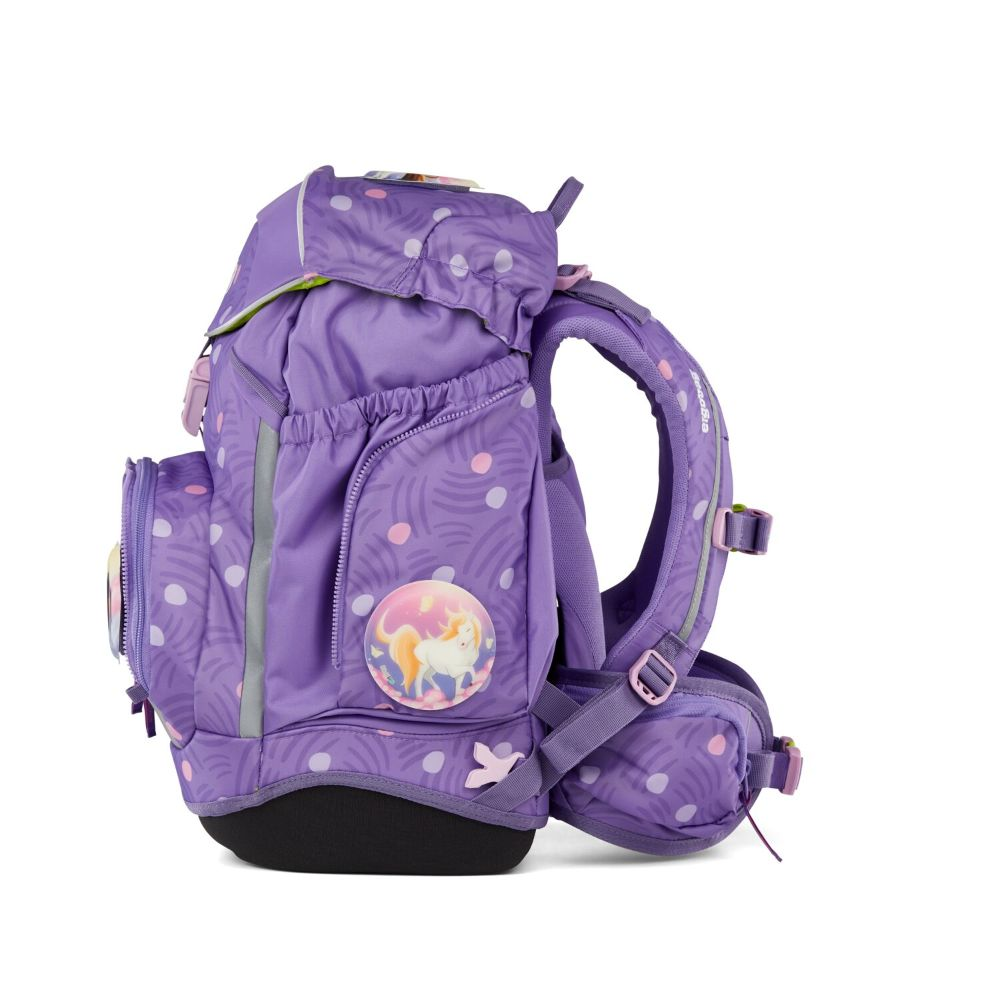 Ein lila Schulrucksack mit weißen Punkten, einem Einhorn-Patch und schwarzem Boden. Er hat zwei Gurte und mehrere Taschen.