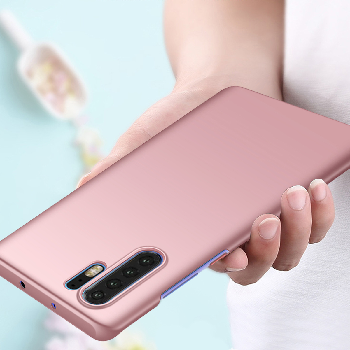 Eine Hand hält ein roségoldenes Telefon. Das Telefon hat mehrere Kameras. Ein weißes Hemd und eine verschwommene Kelle sind im Hintergrund.