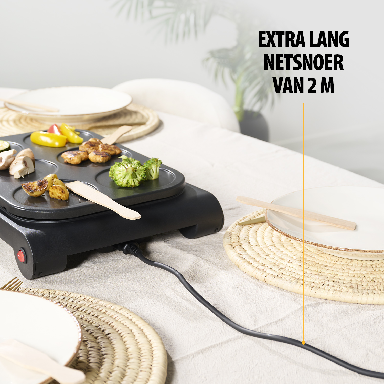 Ein Raclette-Grill mit Gemüse. Teller, Tischsets und ein langes Netzkabel sind auf einem Tisch. Text: EXTRA LANG NETSNOER VAN 2 M.