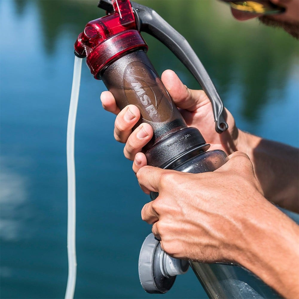 Eine Person benutzt einen Wasserfilter. Der Filter ist schwarz und rot. Wasser fließt aus einem weißen Schlauch. Wasser ist im Hintergrund.