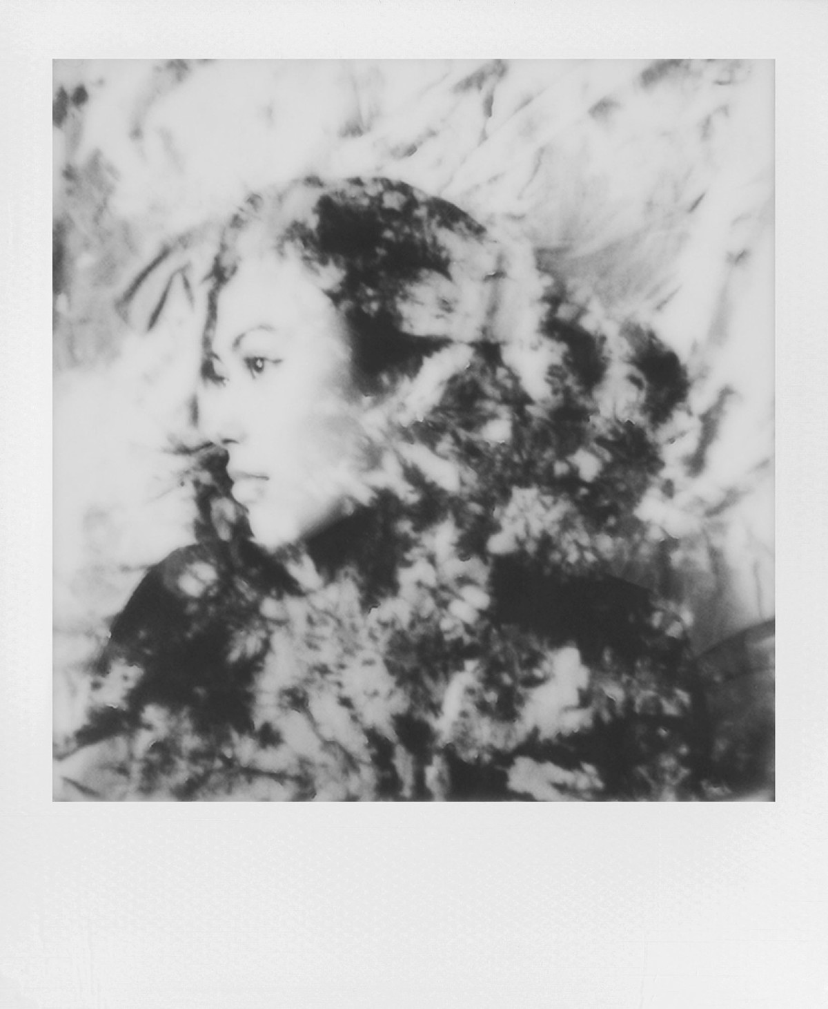 Czarno-białe zdjęcie przedstawia profil kobiety otoczony wzorem ciemnych i jasnych kształtów, przypominających liście lub tkaninę.