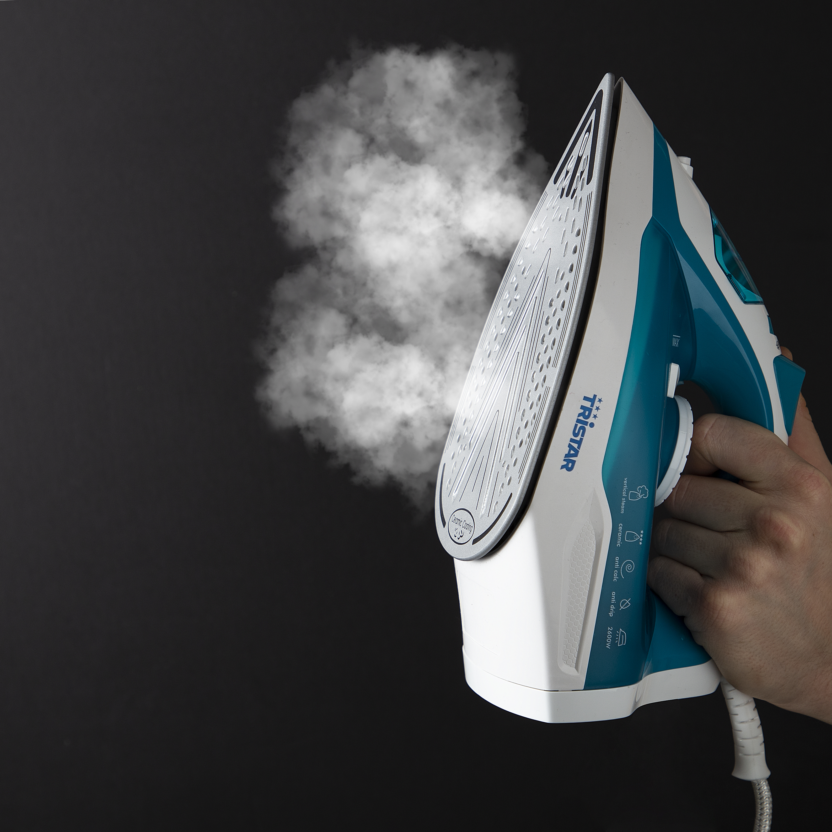 Ręka trzymająca biało-zielone żelazko z wydobywającą się parą. Czarne tło.