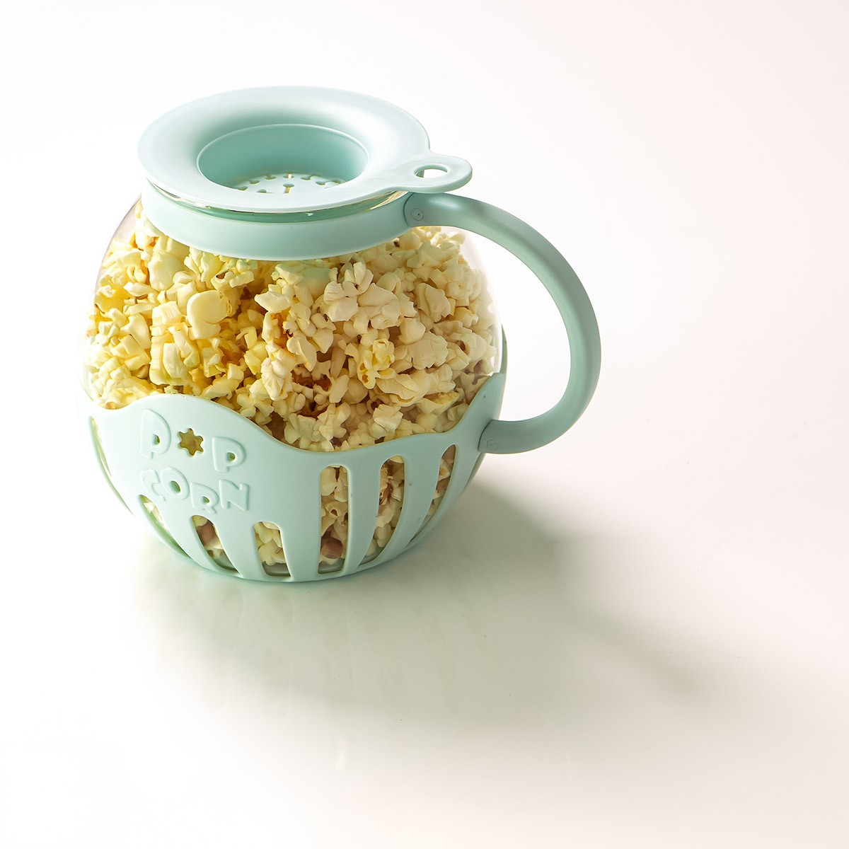 Una macchina per popcorn piena di popcorn. La macchina è azzurra con manico e coperchio, su una superficie bianca.