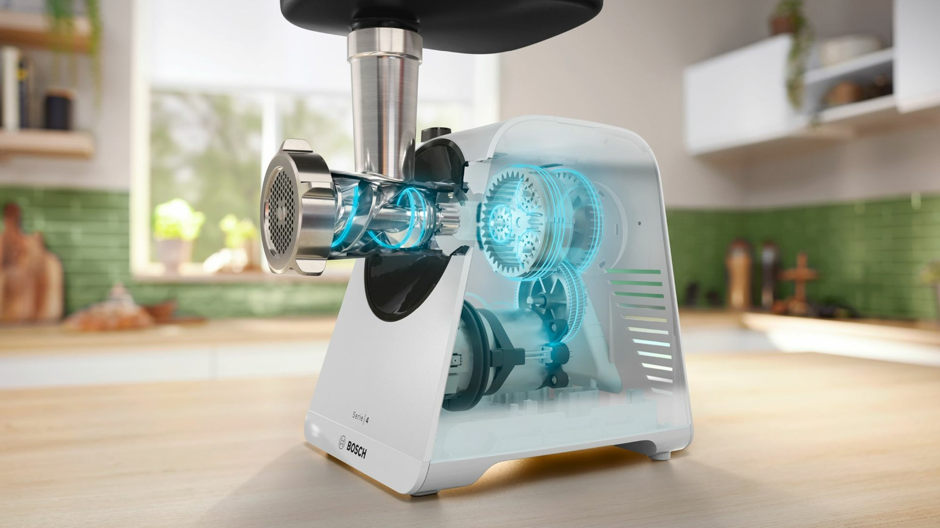 Biała maszynka do mielenia mięsa Bosch z widocznymi wewnętrznymi kołami zębatymi. Stoi na drewnianym blacie w kuchni z zielonymi płytkami.