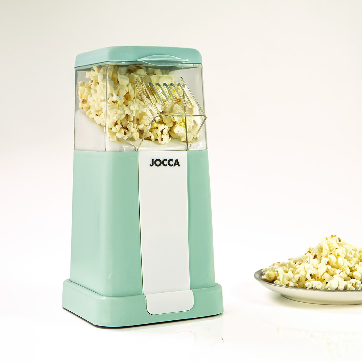 Una macchina per popcorn verde menta con popcorn all'interno e un piatto di popcorn accanto. Il marchio JOCCA è visibile.