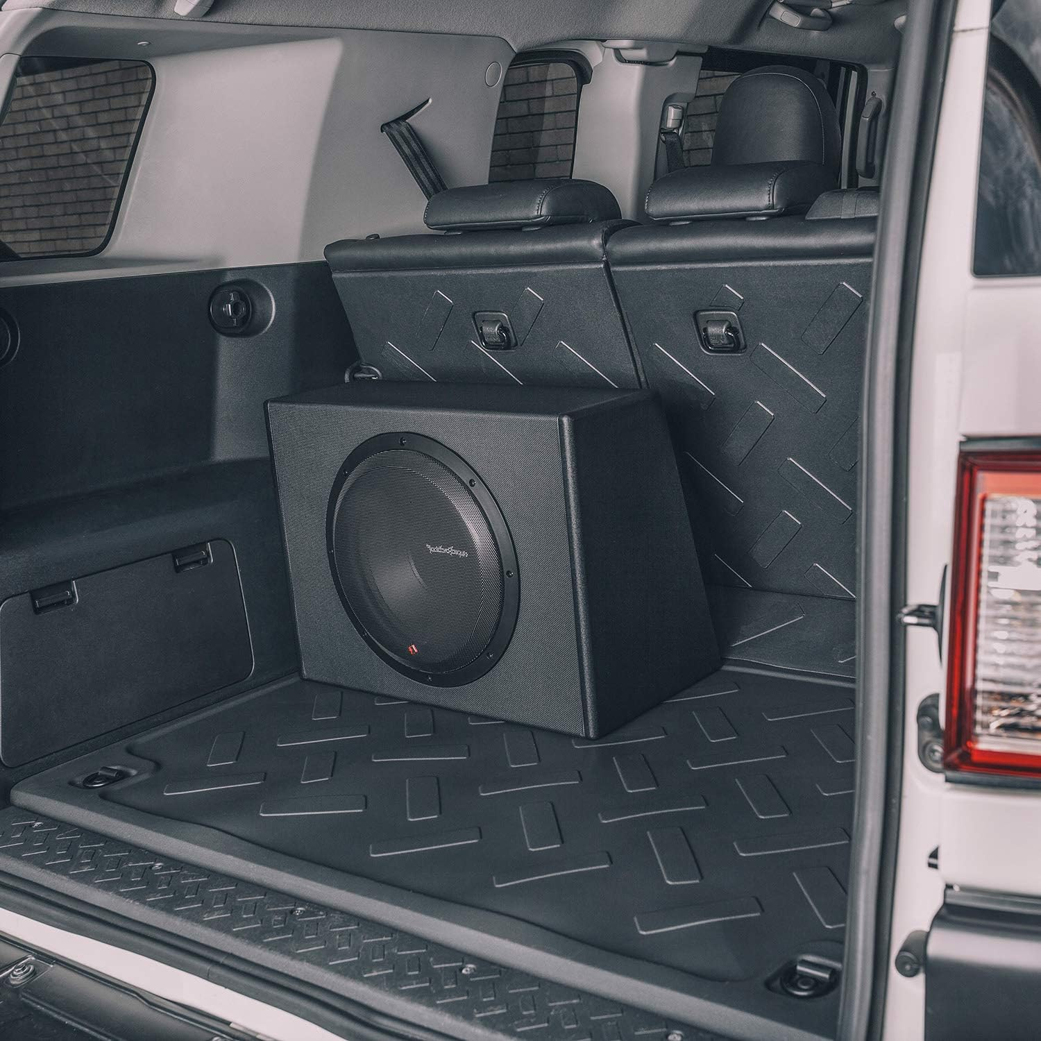 Innenraum des Kofferraums mit einer Subwoofer-Box. Schwarzer Lautsprecher, schwarze Paneele und ein schwarzer Boden. Das Auto ist weiß.