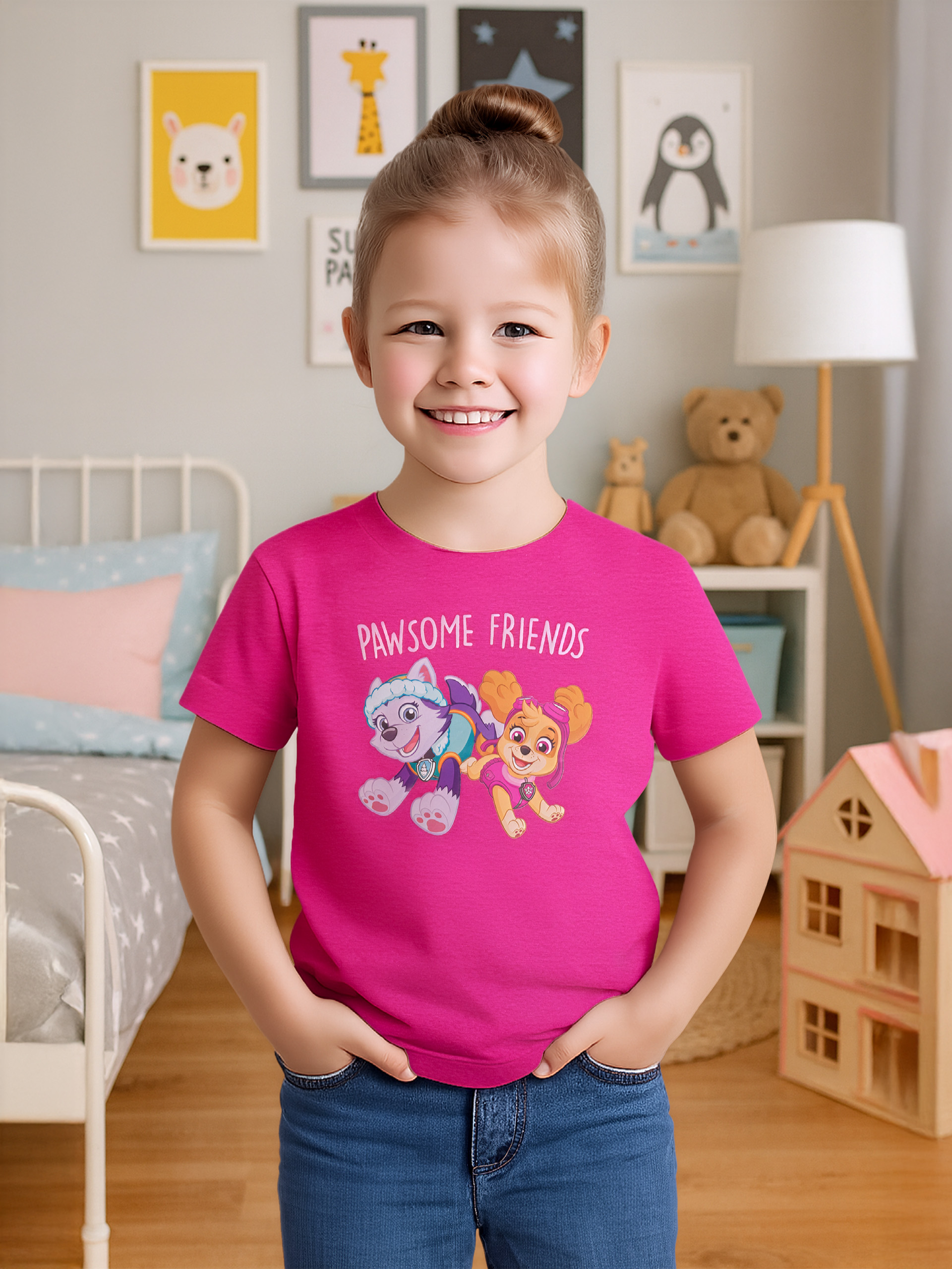 Ein lächelndes Mädchen trägt ein pinkes T-Shirt mit Paw Patrol-Figuren. Sie ist in einem Raum mit Zeichnungen an der Wand.