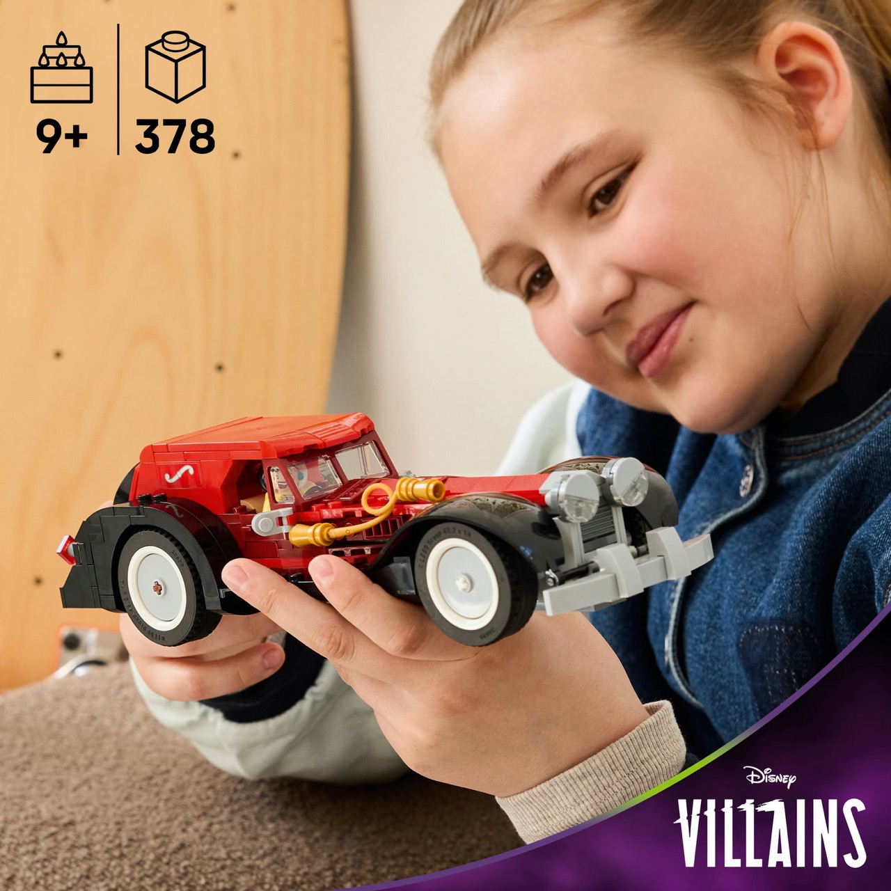 Een meisje glimlacht en houdt een rode Lego-auto vast. De auto heeft zwarte wielen en gouden accenten. Achtergrond toont leeftijd en aantal stukjes.