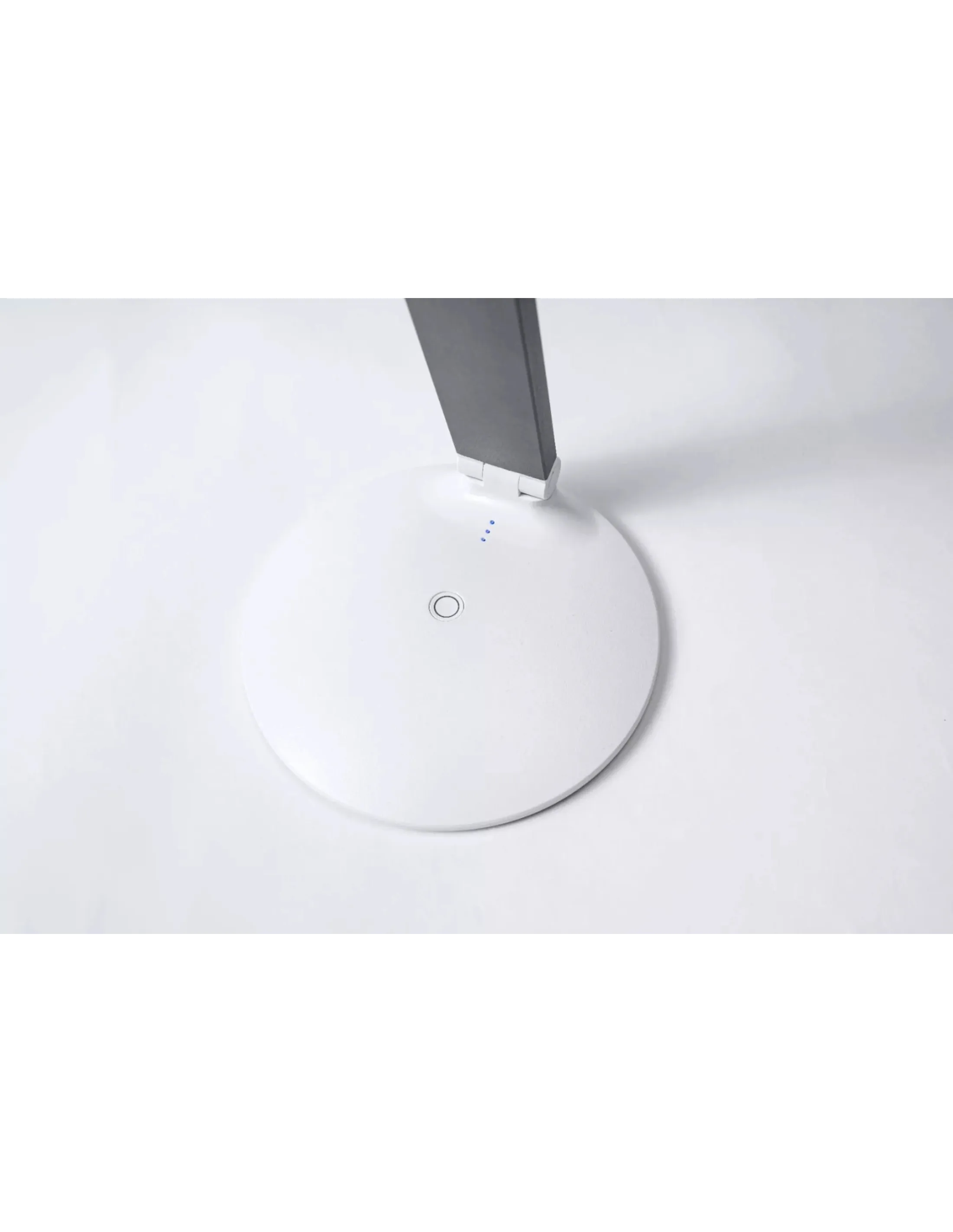 Een witte bureaulamp met een ronde basis en een grijze arm staat op een wit oppervlak.