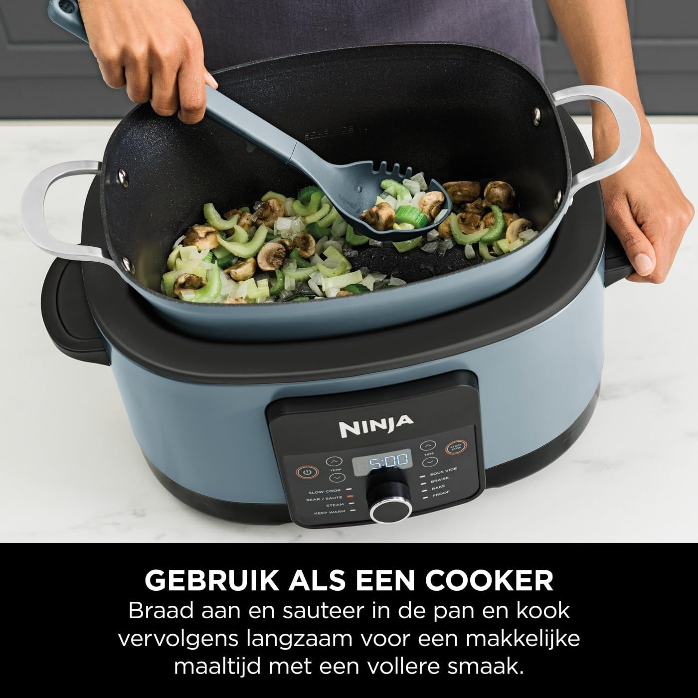 Een persoon roert groenten en champignons met een grijze lepel in een blauwe Ninja-kookpot. De kookpot heeft een digitaal display.