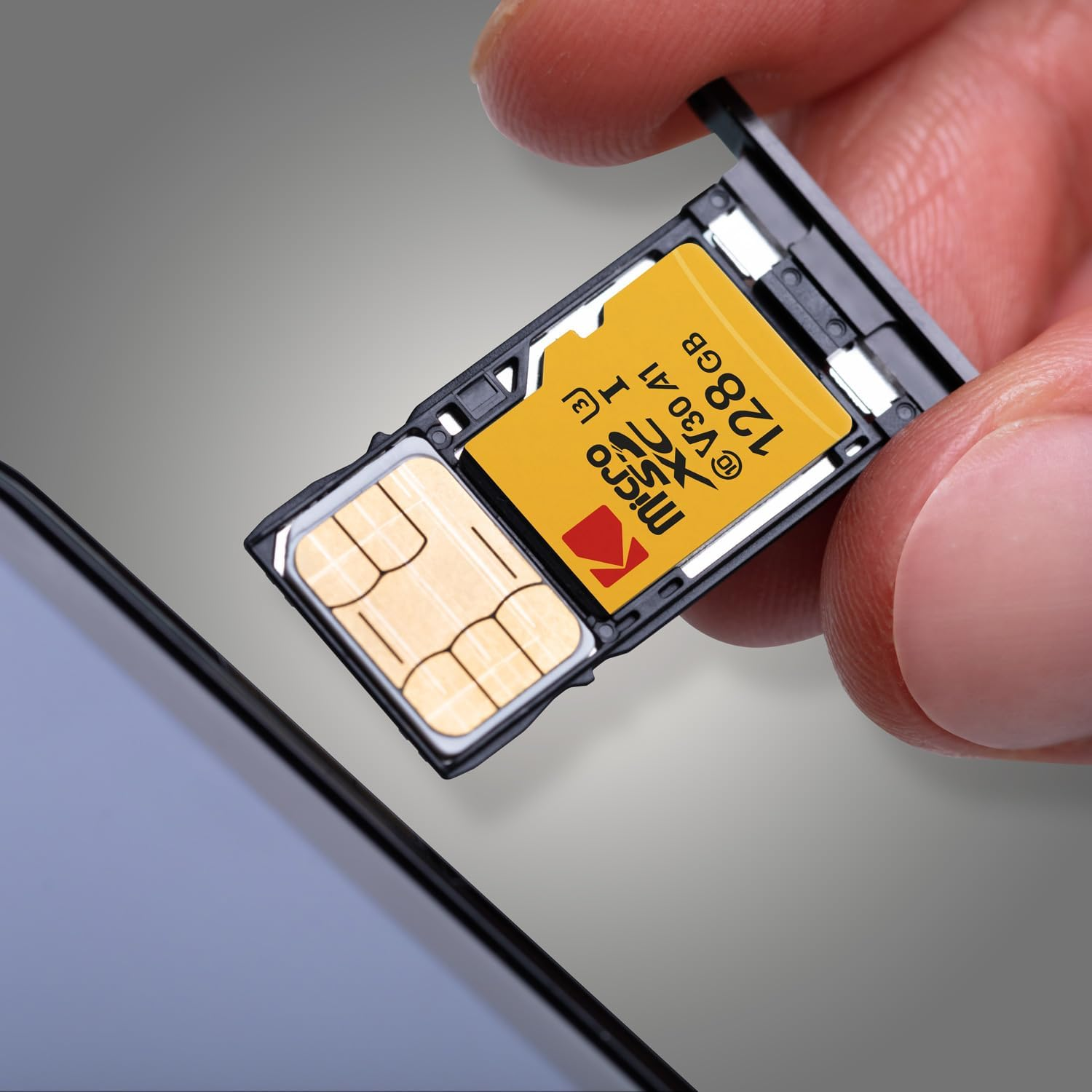 Eine Hand setzt eine gelbe und schwarze Micro-SD-Karte mit 128 GB Kapazität in ein Telefon ein. Die Karte ist mit Kodak beschriftet.