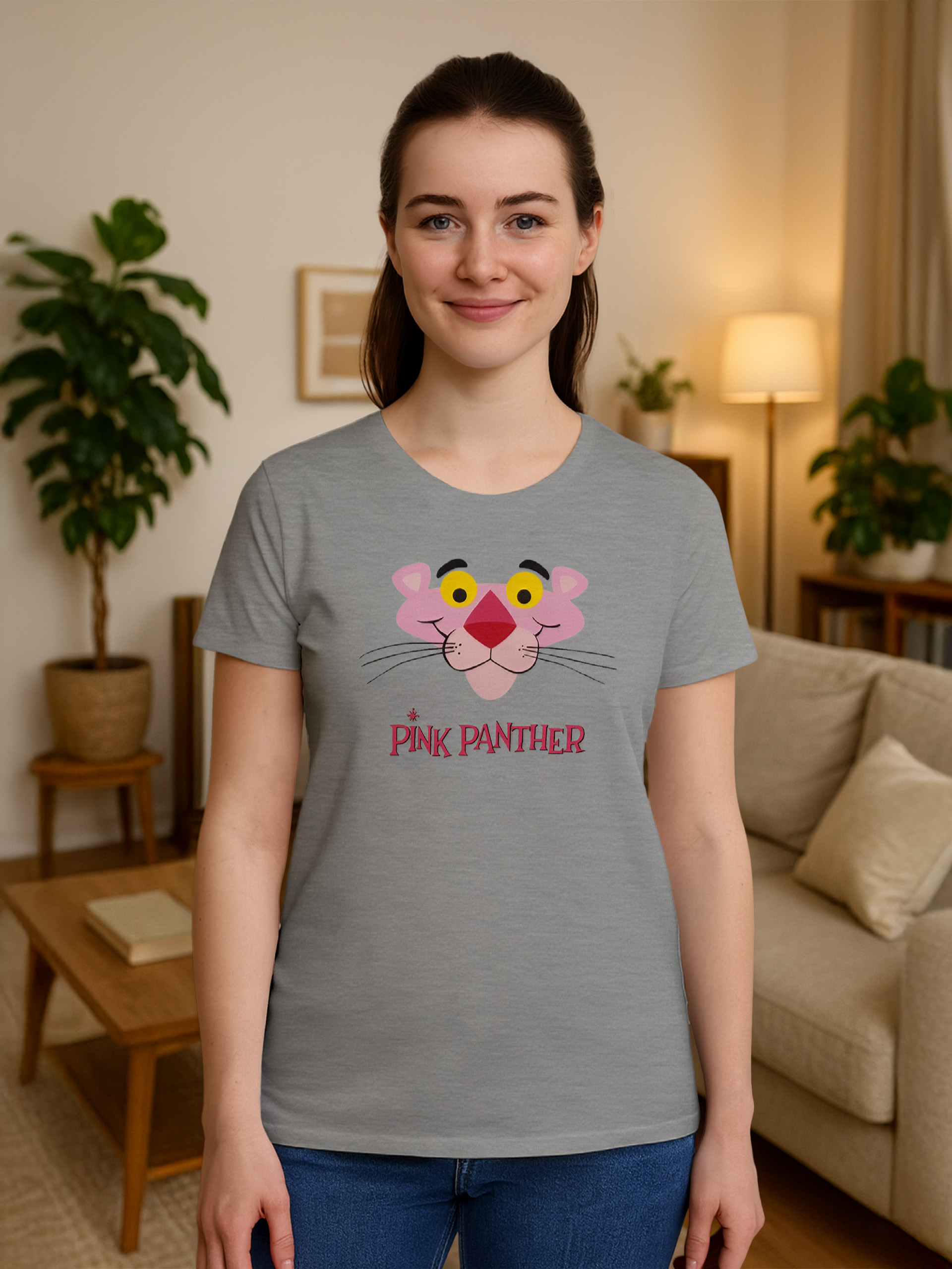 Eine Frau trägt ein graues T-Shirt mit einem Pink-Panther-Design. Sie lächelt in einem Wohnzimmer.