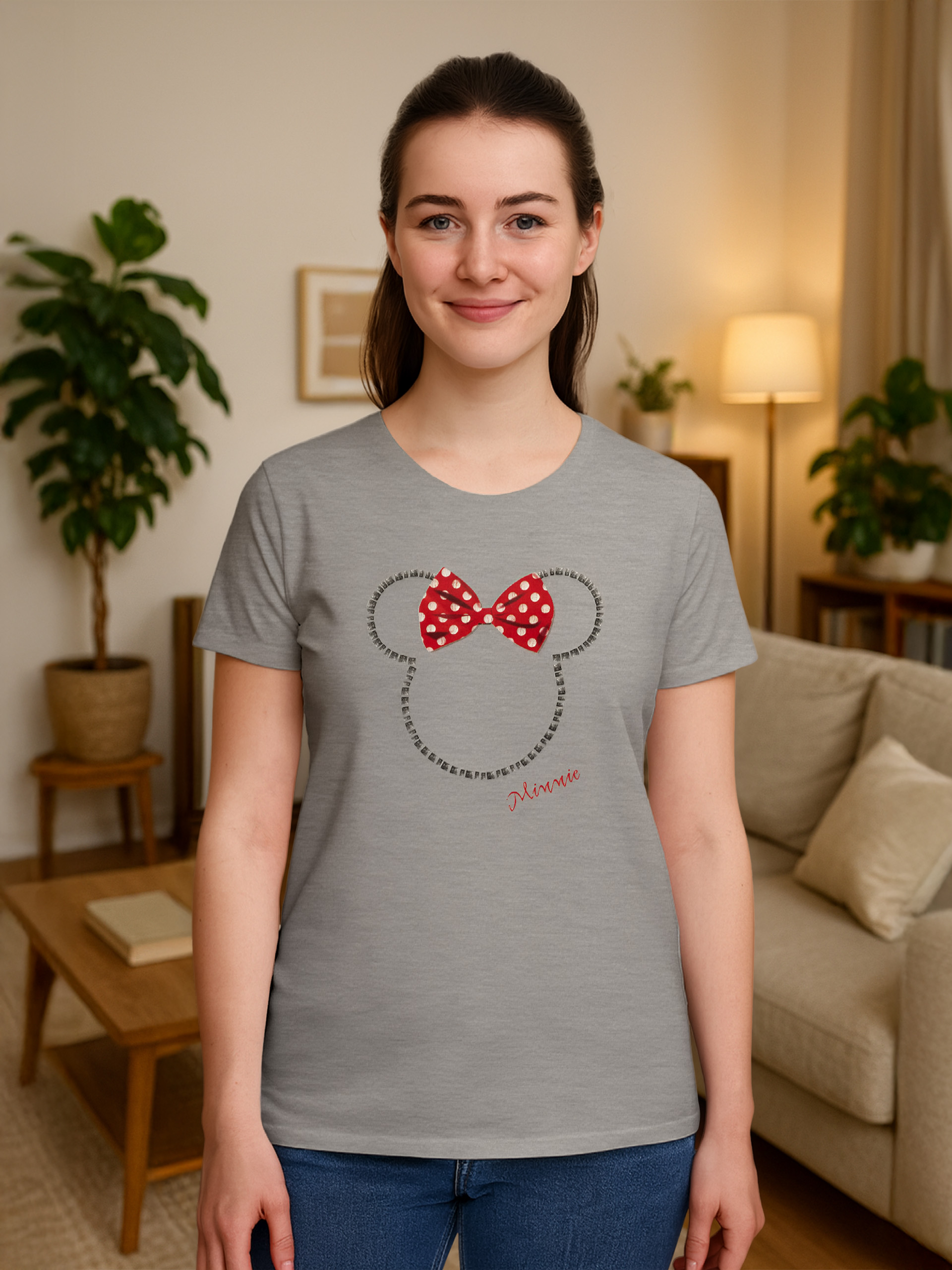 Eine Frau mit einem grauen Minnie-Maus-T-Shirt lächelt. Hintergrund: Pflanzen, Sofa, Tisch, Lampe.
