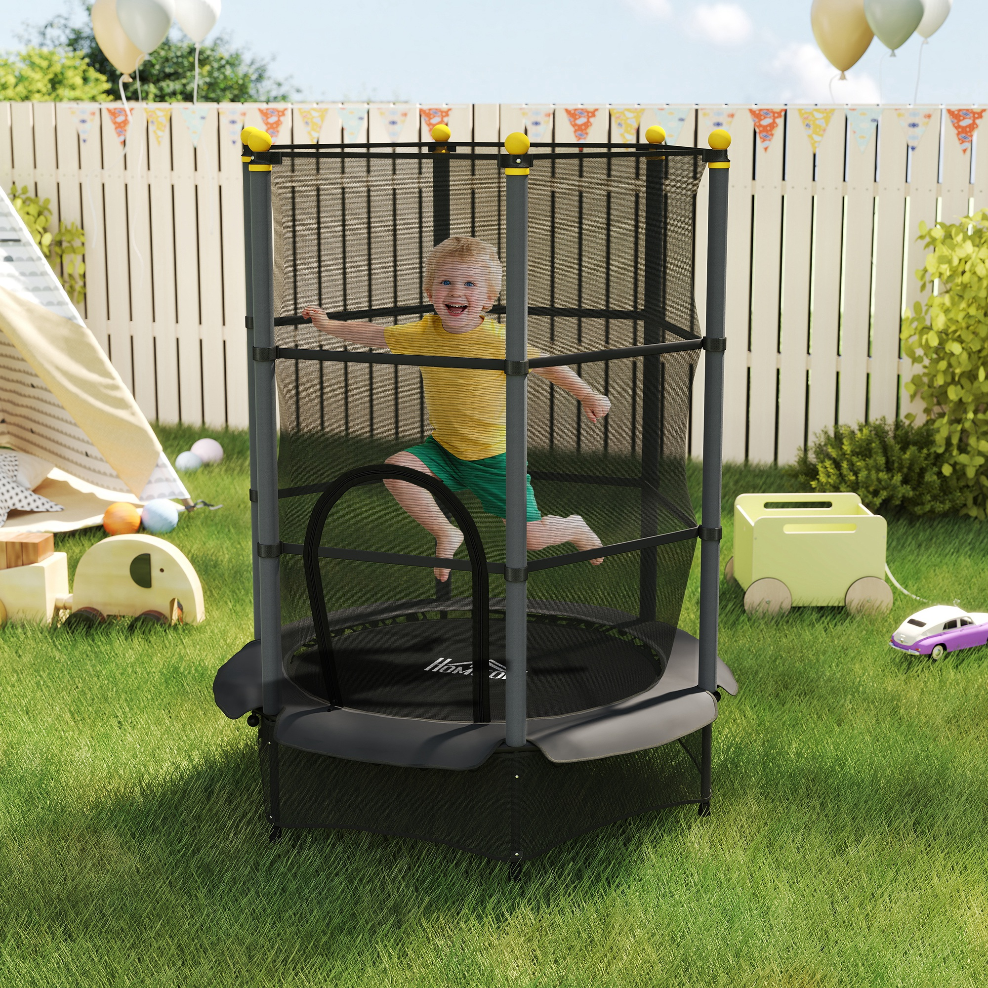 Un bambino salta su un trampolino in un cortile. Palloncini, una recinzione e giocattoli sullo sfondo.