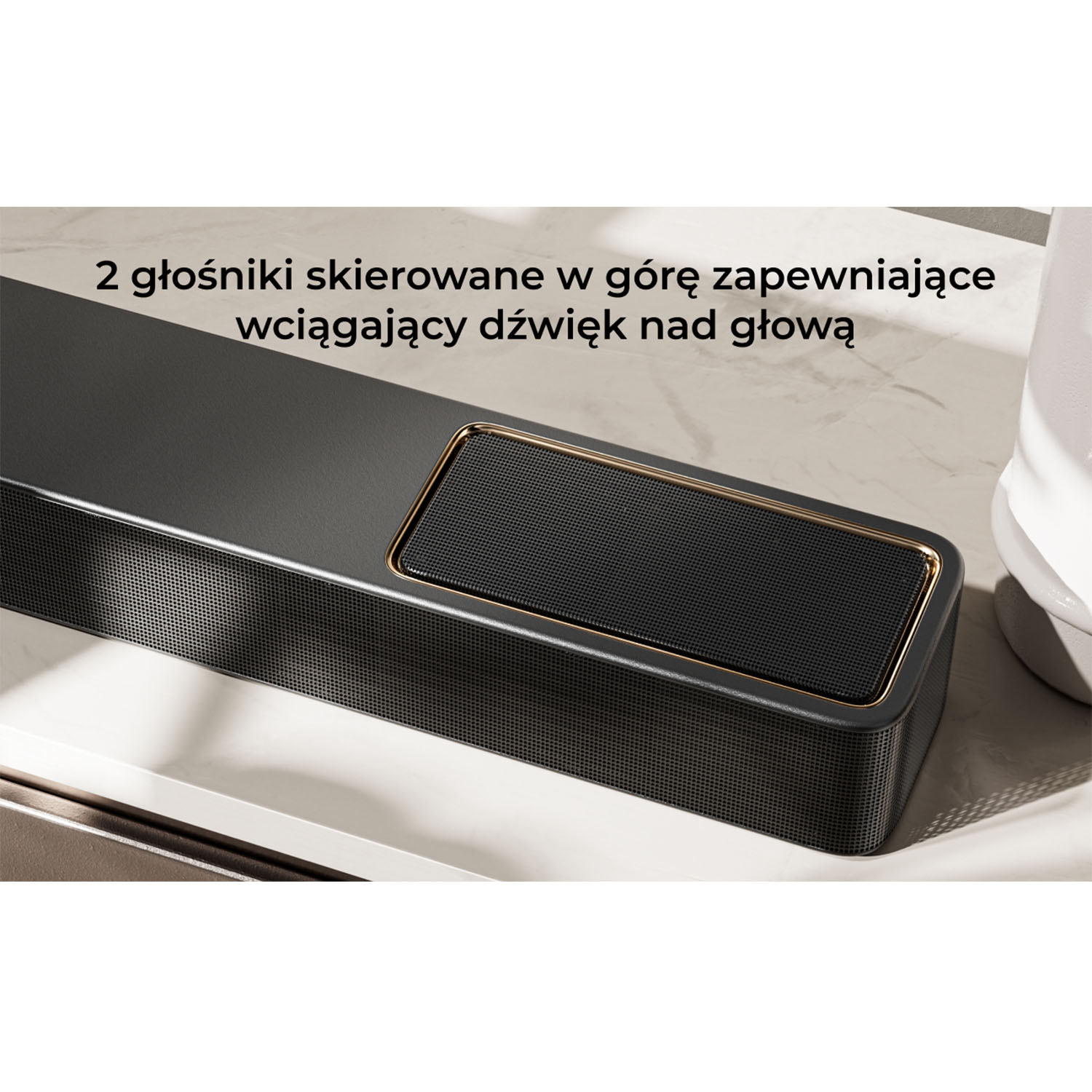 Zbliżenie czarnego soundbaru ze złotą ramą i siatkowym detalem, umieszczonego na białej powierzchni, z białym wazonem.