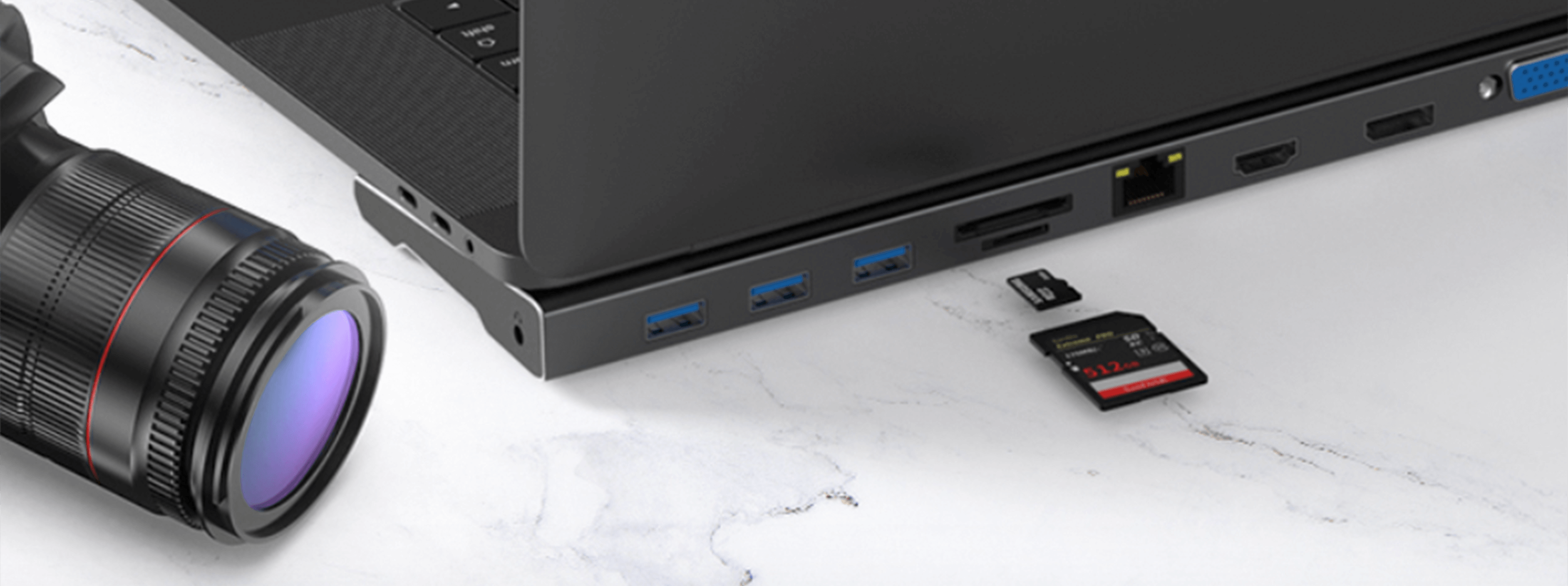 Laptop z kartami SD i obiektywem aparatu na marmurowej powierzchni. Laptop ma porty USB i inne złącza.