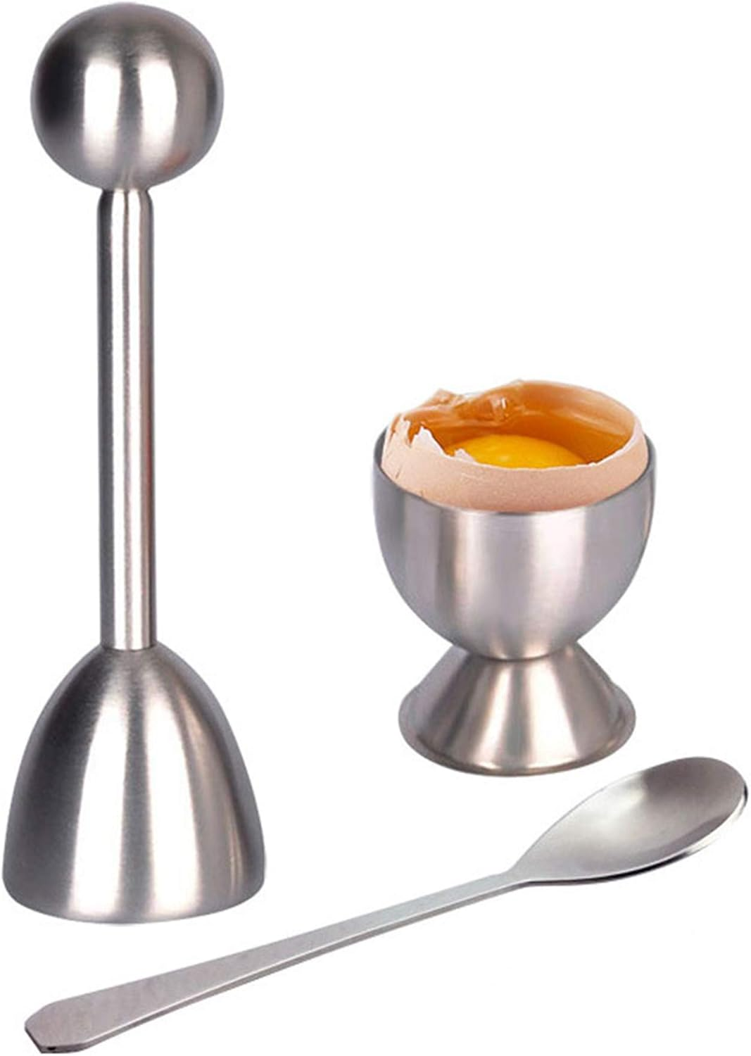 Auf einer weißen Oberfläche befinden sich ein Eierknacker aus Edelstahl, ein Eierbecher mit Ei und ein Löffel. Das Ei hat eine zerbrochene Schale.