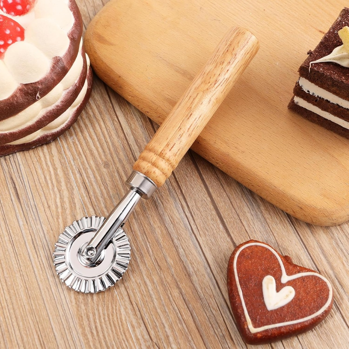 Ein Teigschneider mit Holzgriff liegt auf einer Holzoberfläche, mit Kuchen und einem herzförmigen Keks.