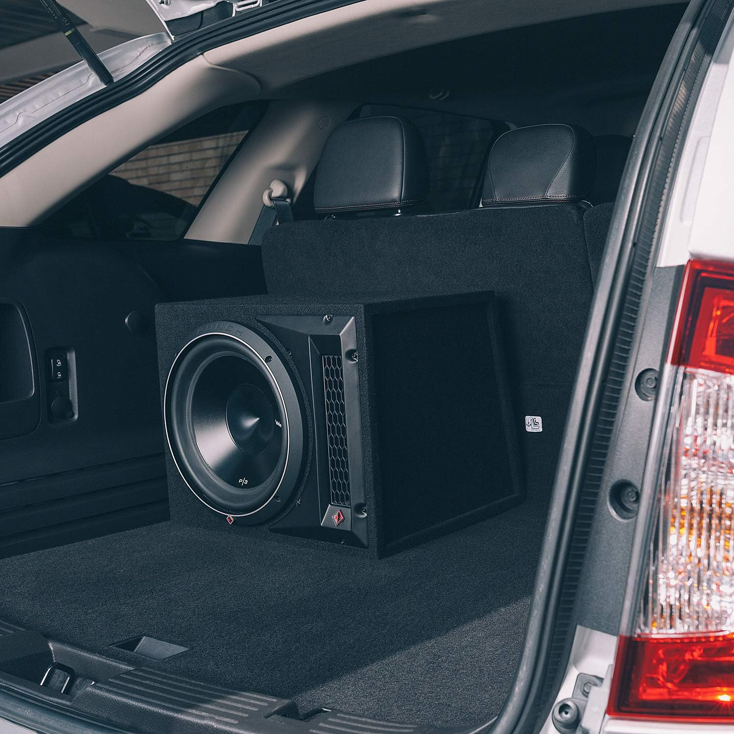 Ein Kofferraum mit einem eingebauten schwarzen Subwoofer. Der Kofferraum ist geöffnet und zeigt den Lautsprecher und den Innenraum des Autos.