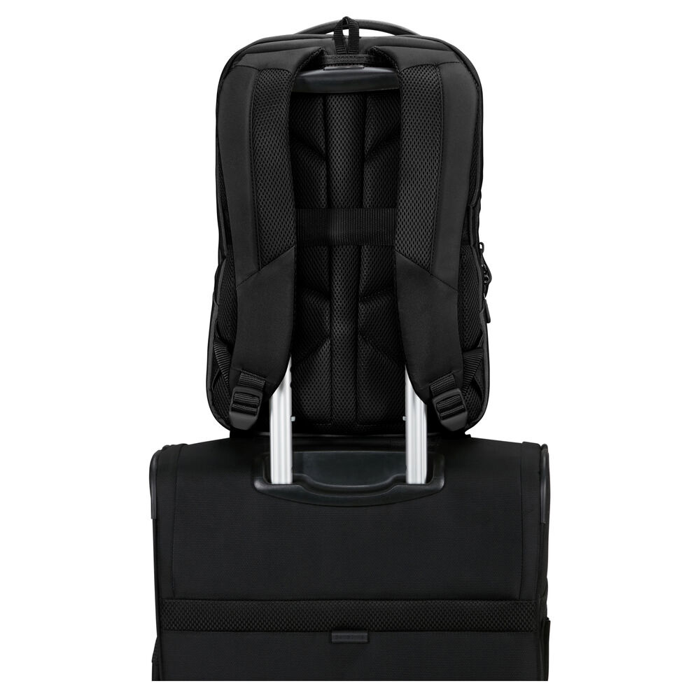 Ein schwarzer Rucksack liegt auf einem schwarzen Rollkoffer. Der Rucksack hat gepolsterte Gurte, und der Griff des Koffers ist sichtbar.