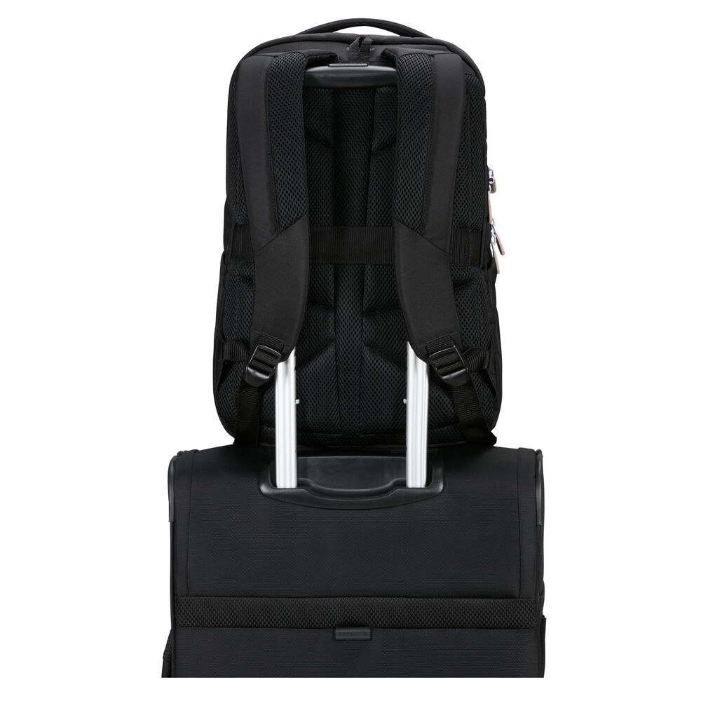 Ein schwarzer Rucksack steht auf einem schwarzen Rollkoffer. Beide werden von hinten betrachtet. Der Rucksack hat Träger und einen Griff. Der Koffer hat einen Griff.