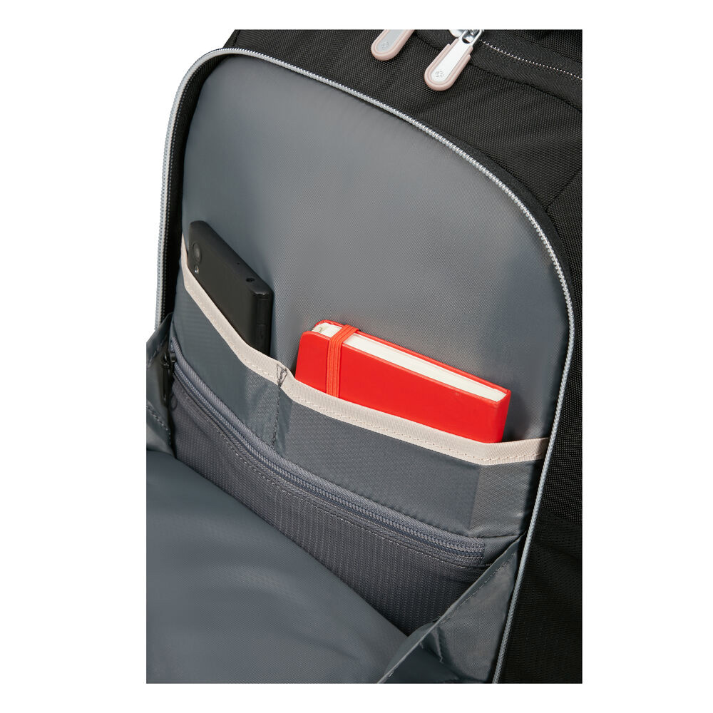 In einem schwarzen Rucksack. Ein rotes Notizbuch und ein schwarzes Telefon befinden sich in den grauen Taschen. Der Hintergrund ist grau.