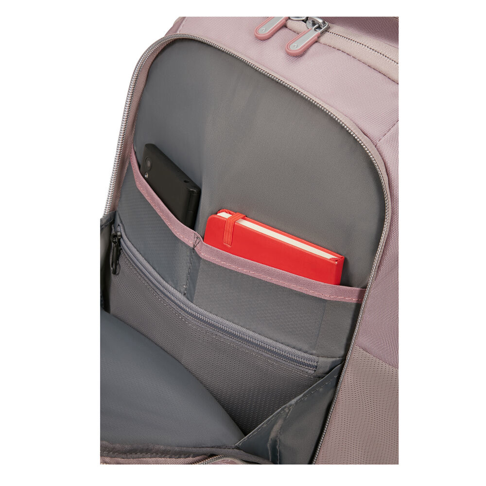 Nahaufnahme einer rosafarbenen Rucksacktasche. Ein schwarzes Telefon und ein rotes Notizbuch sind sichtbar. Der Hintergrund ist grau.