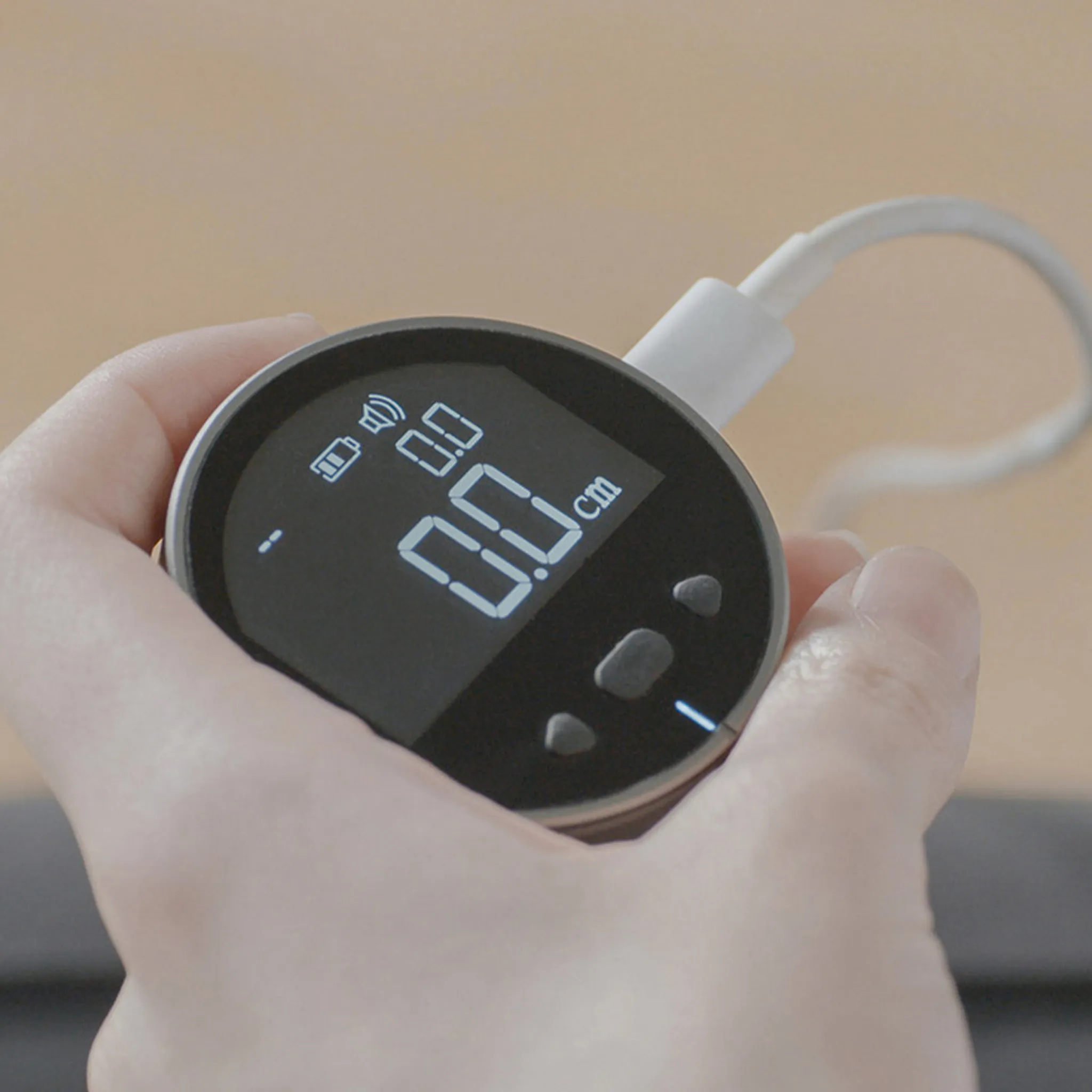 Eine Hand hält ein schwarzes digitales Messwerkzeug, das 0,0 cm anzeigt. Ein weißes Kabel ist angebracht. Der Hintergrund ist unscharf.