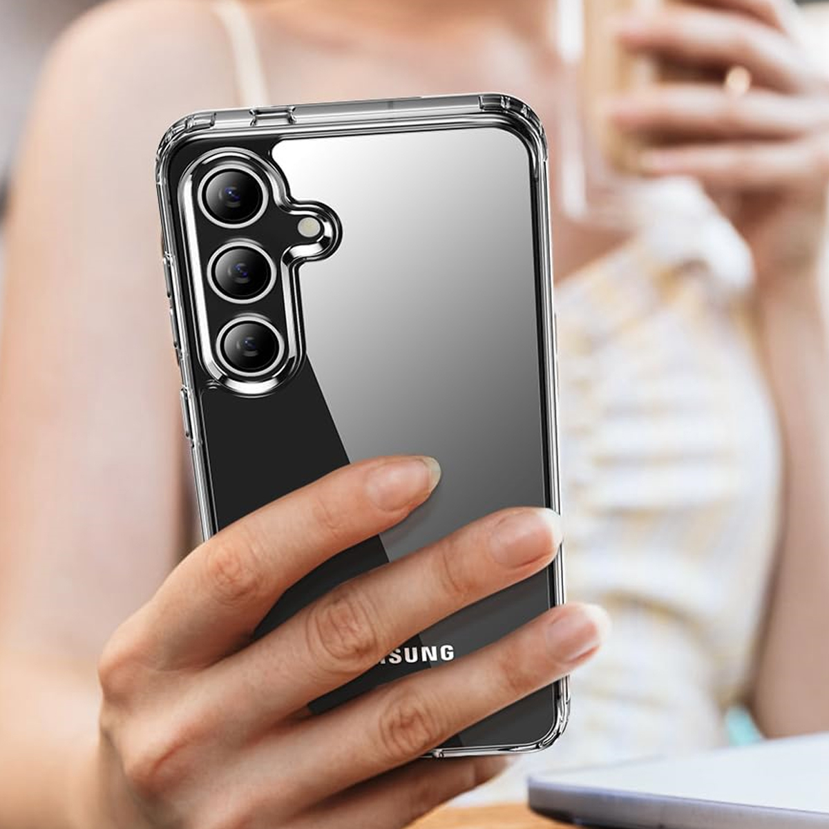 Eine Person hält ein Telefon in einer durchsichtigen Hülle. Das Telefon hat drei Kameras. Der Hintergrund ist verschwommen.