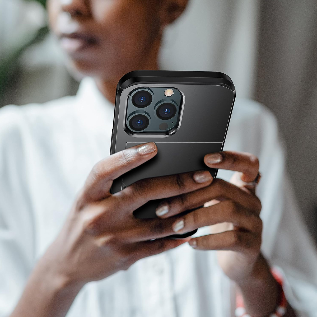 Eine Person hält ein schwarzes Smartphone in einer Hülle mit drei Linsen. Der Hintergrund ist unscharf, ein weißes Hemd.